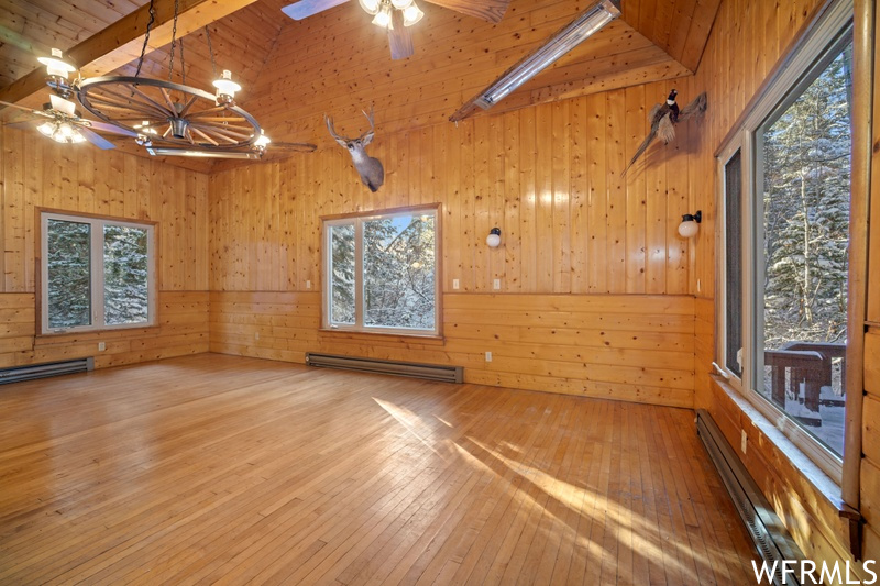 Spare room featuring beamed ceiling, wooden walls, wood ceiling, wood-type flooring, and a baseboard heating unit