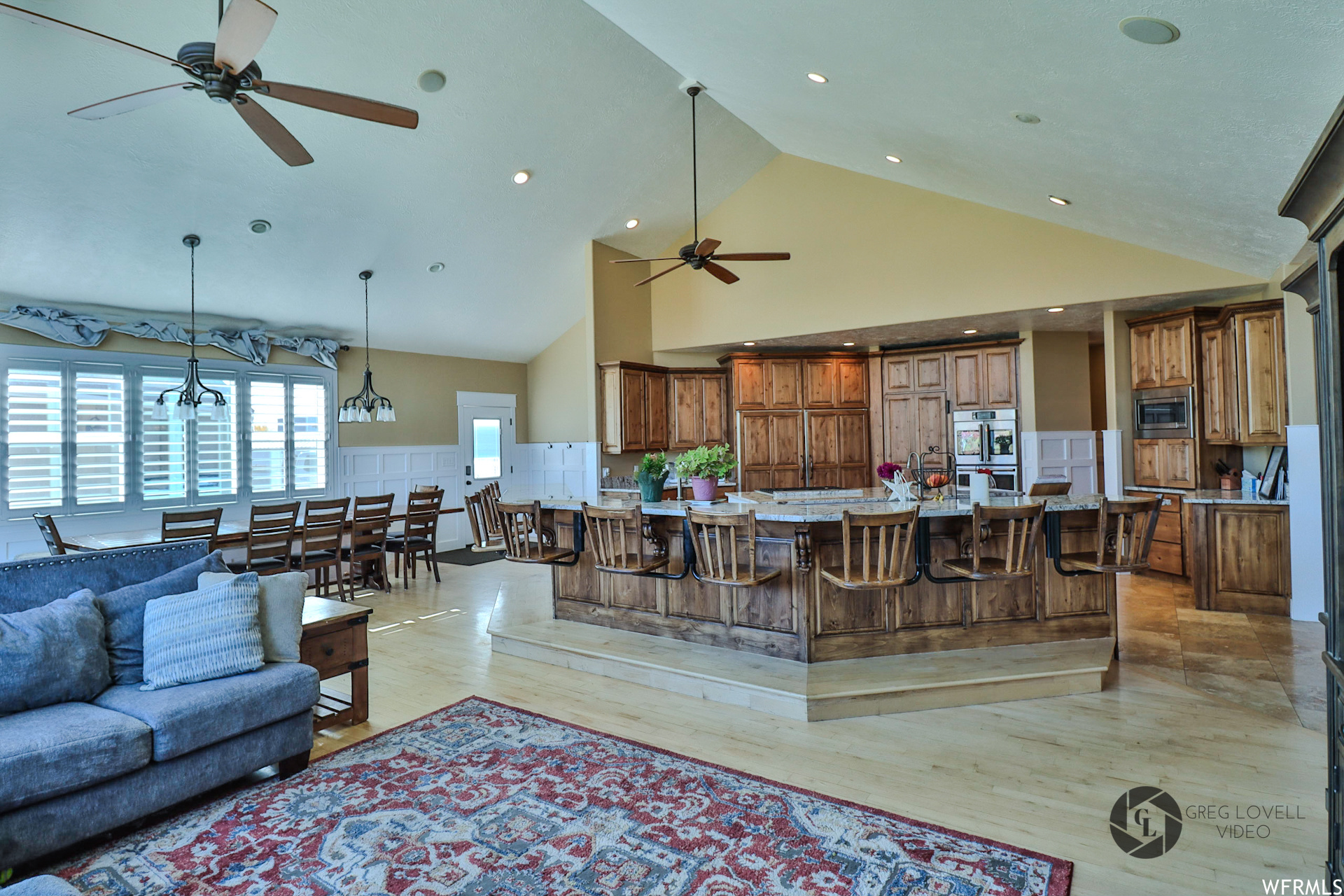 Living room with light hardwood / wood-style floors, ceiling fan with notable chandelier, and high vaulted ceiling