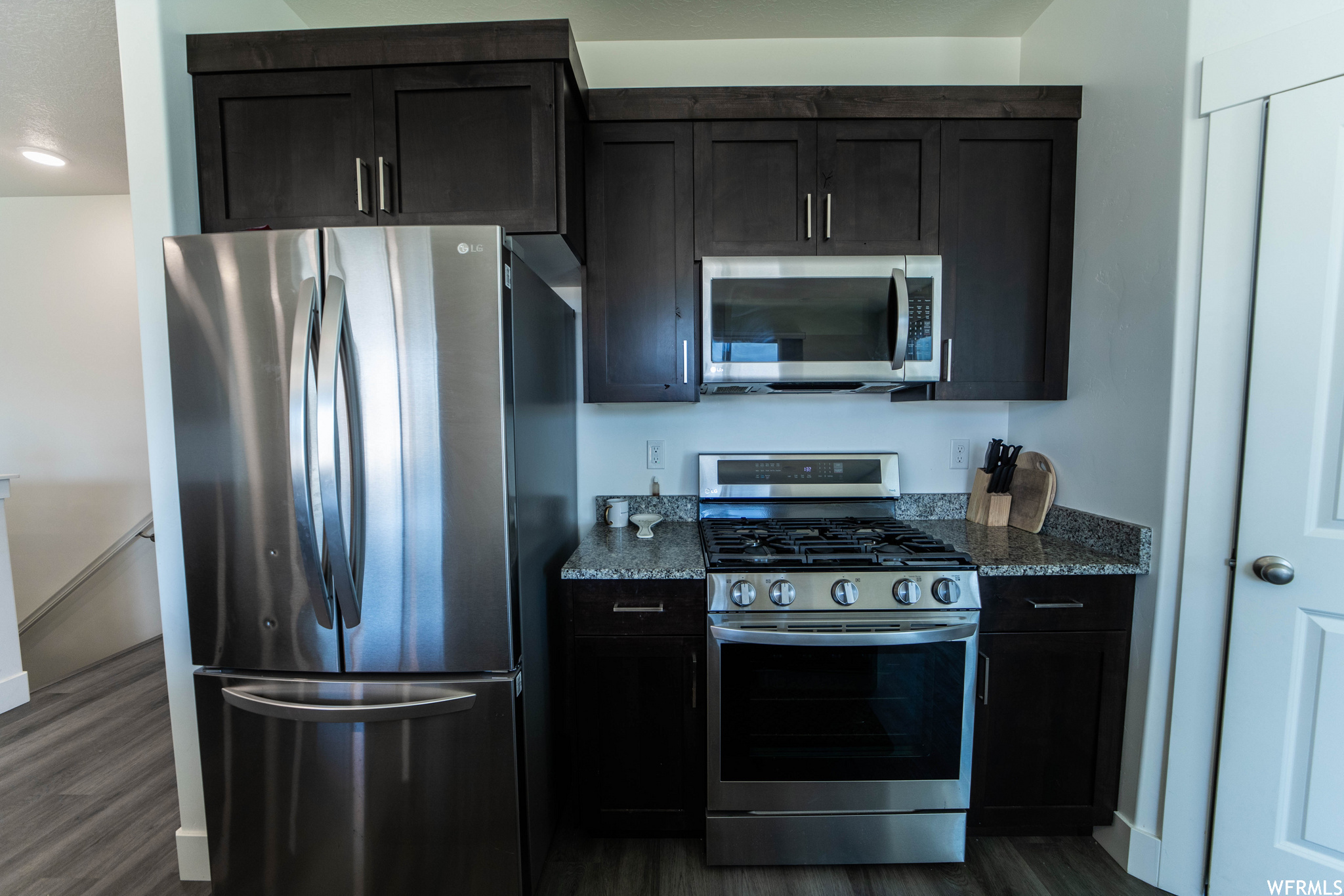 Kitchen with dark hardwood / wood-style flooring, dark stone countertops, and appliances with stainless steel finishes