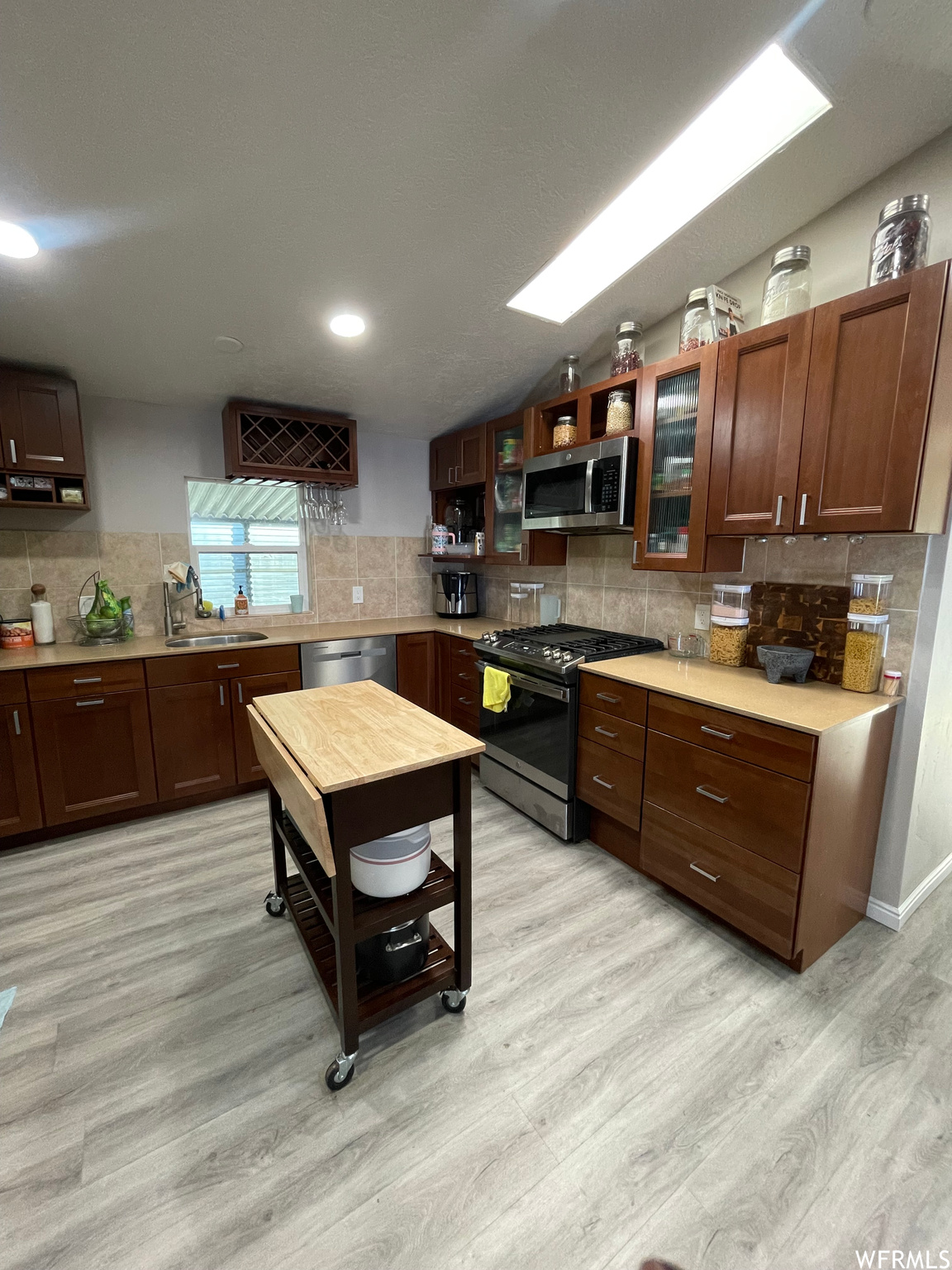 Kitchen with sink, appliances with stainless steel finishes, tasteful backsplash, and light hardwood / wood-style flooring