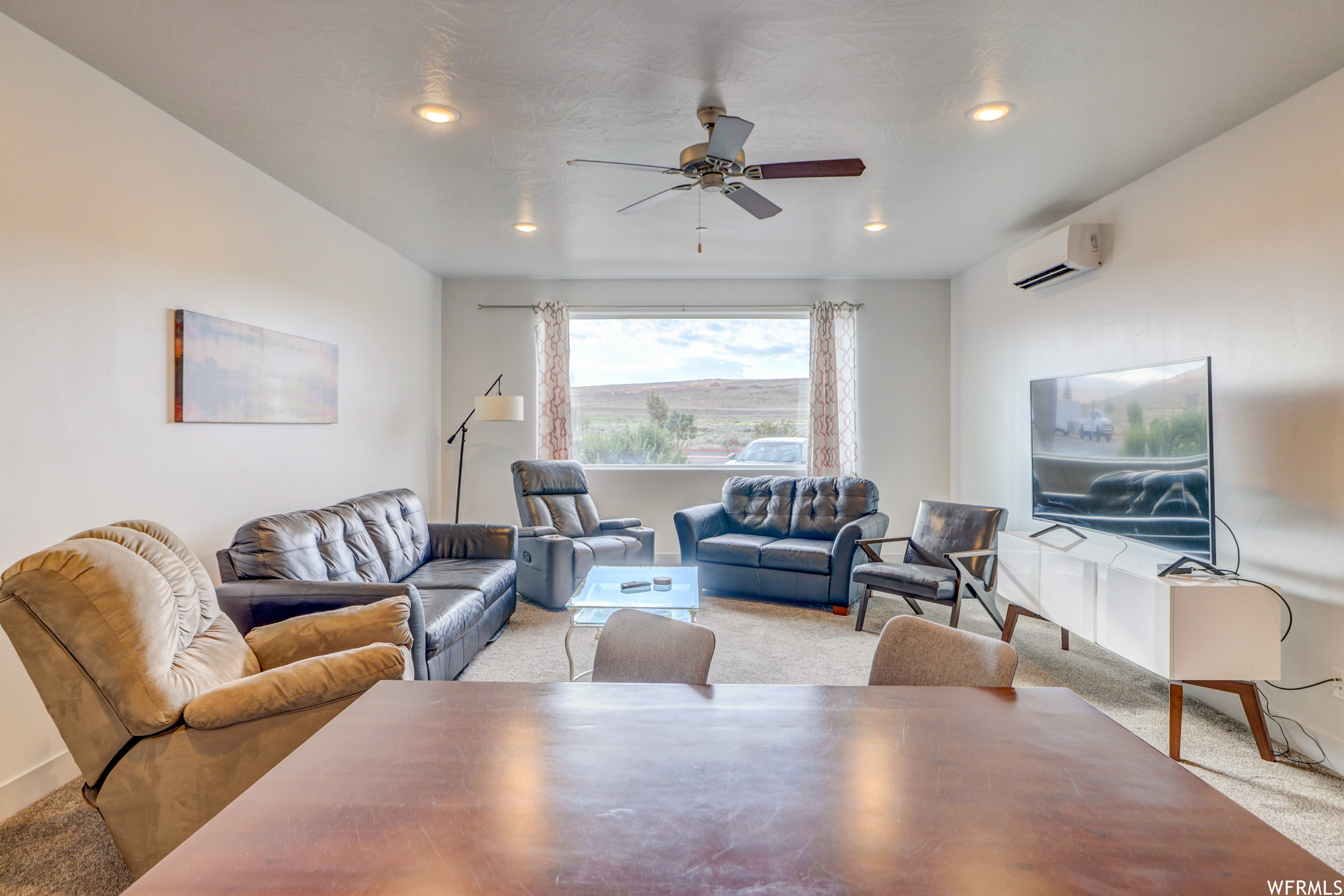 Carpeted living room featuring ceiling fan and a wall mounted air conditioner