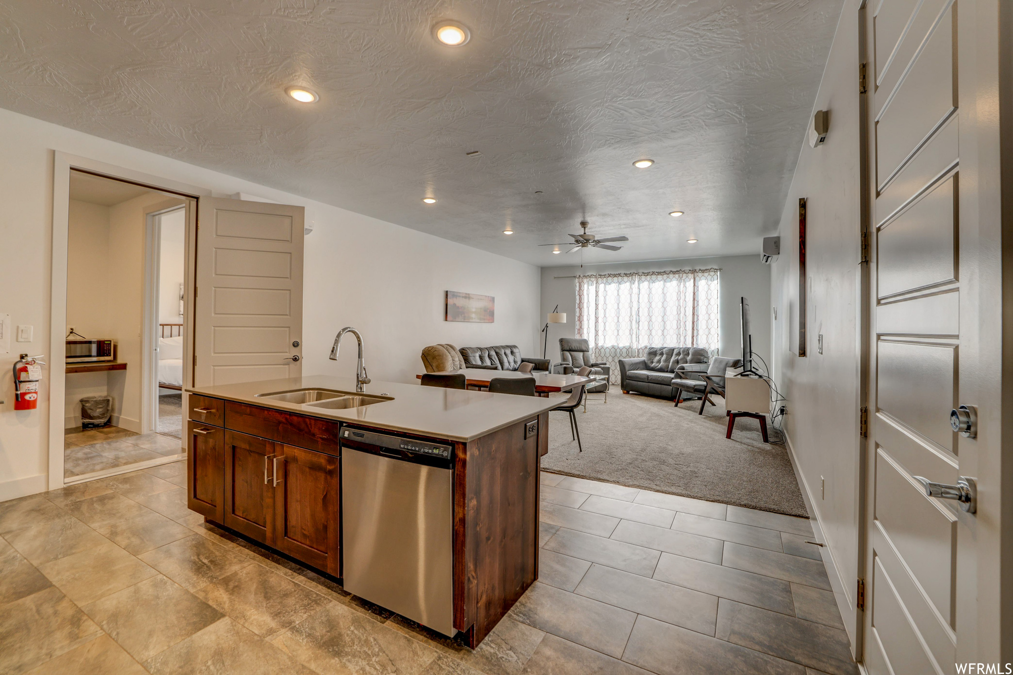 Kitchen featuring light carpet, sink, dishwasher, a center island with sink, and ceiling fan