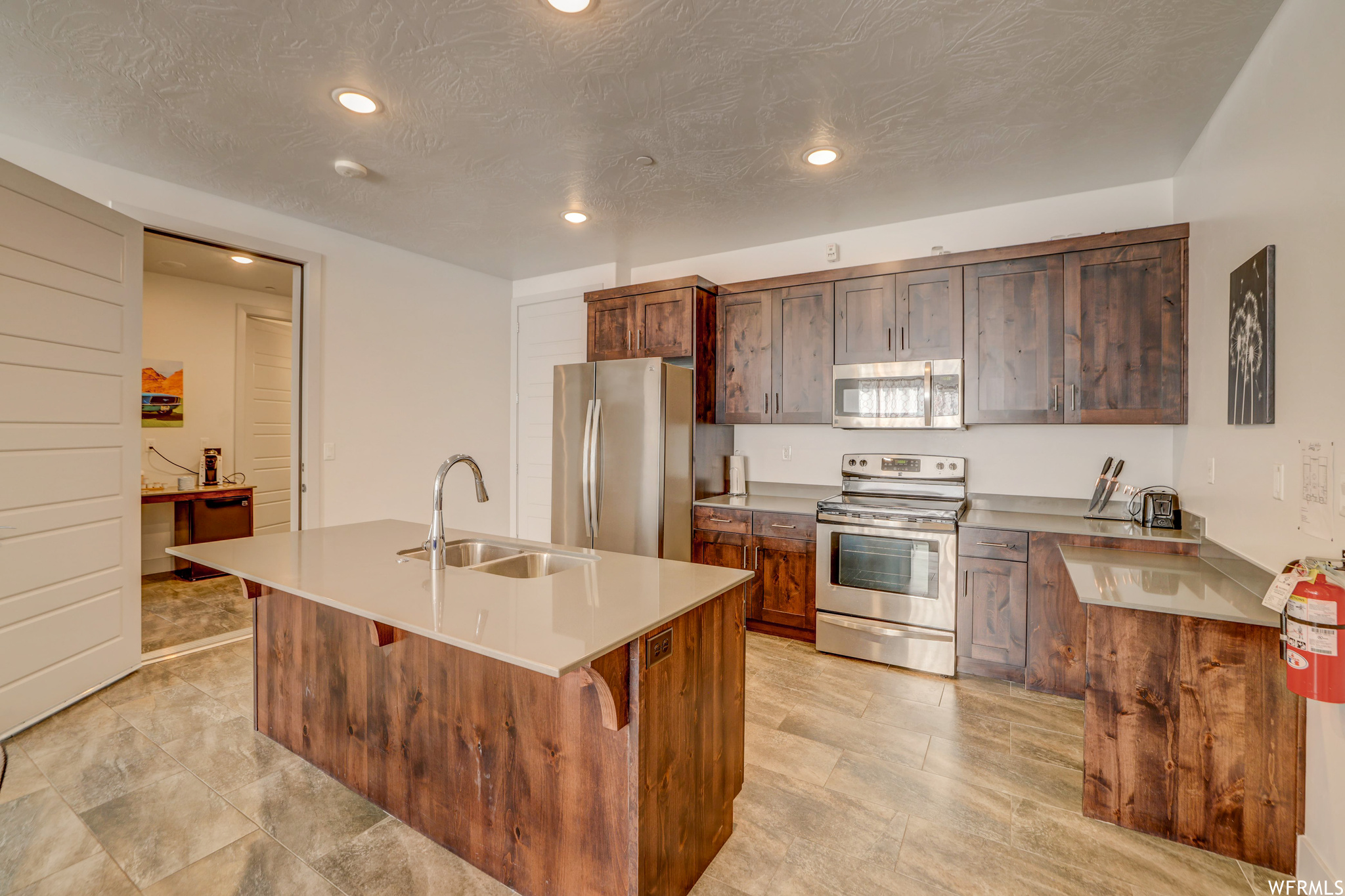 Kitchen with sink, a breakfast bar, an island with sink, light tile flooring, and appliances with stainless steel finishes