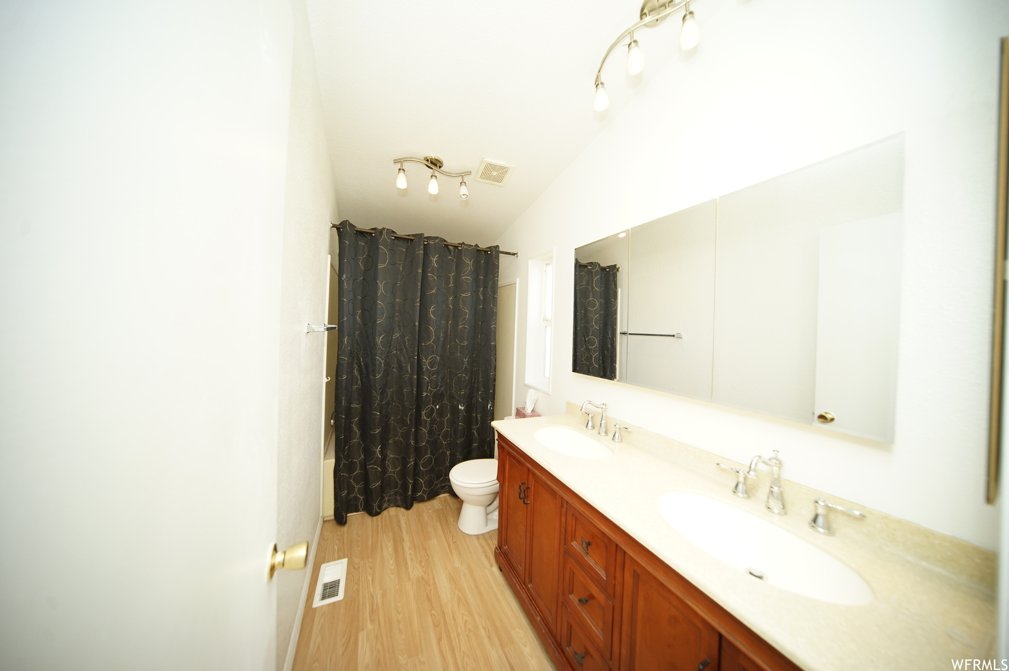 Bathroom with vaulted ceiling, oversized vanity, toilet, double sink, and rail lighting