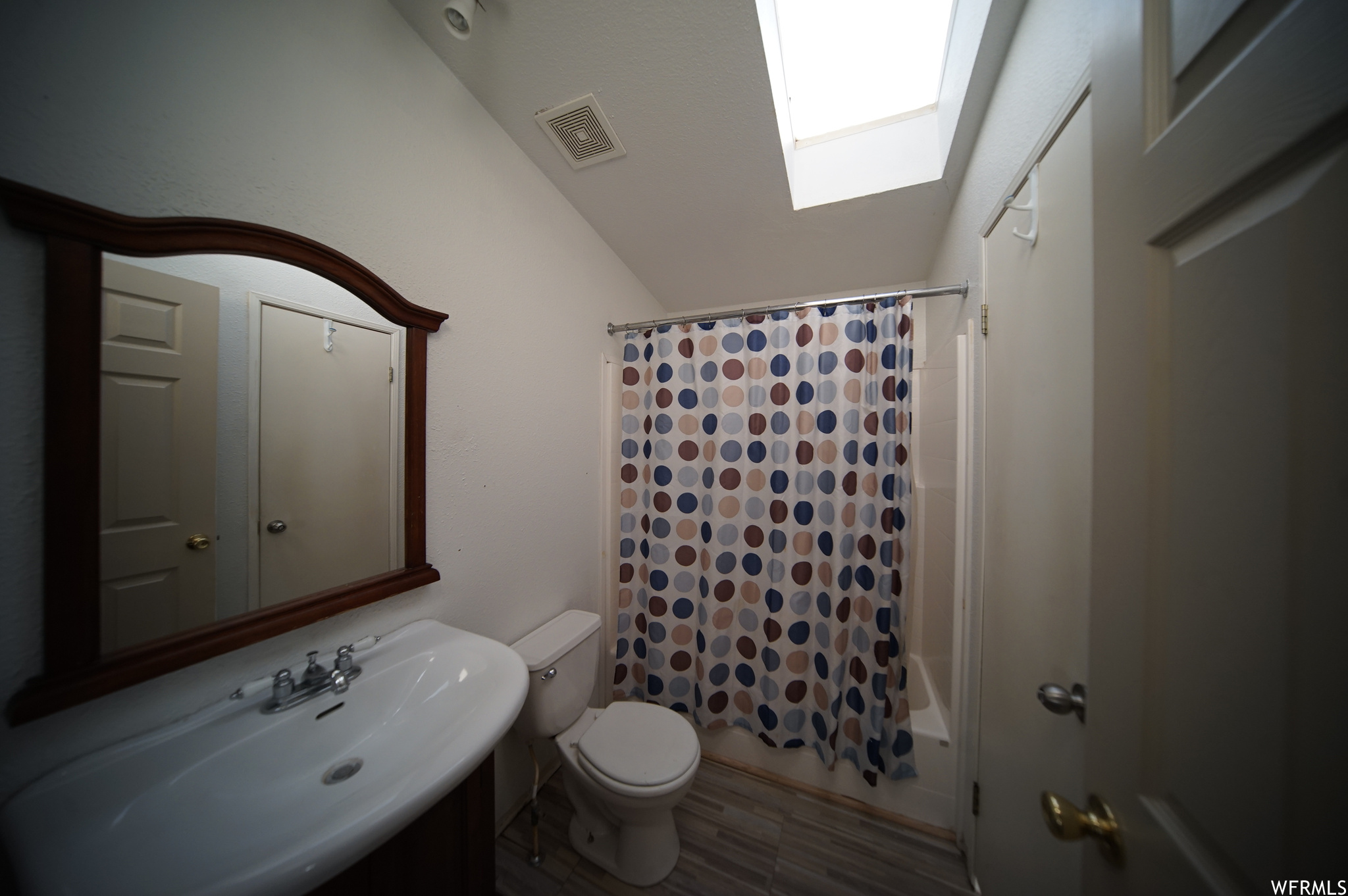 Full bathroom featuring shower / bath combination with curtain, vaulted ceiling with skylight, toilet, and sink