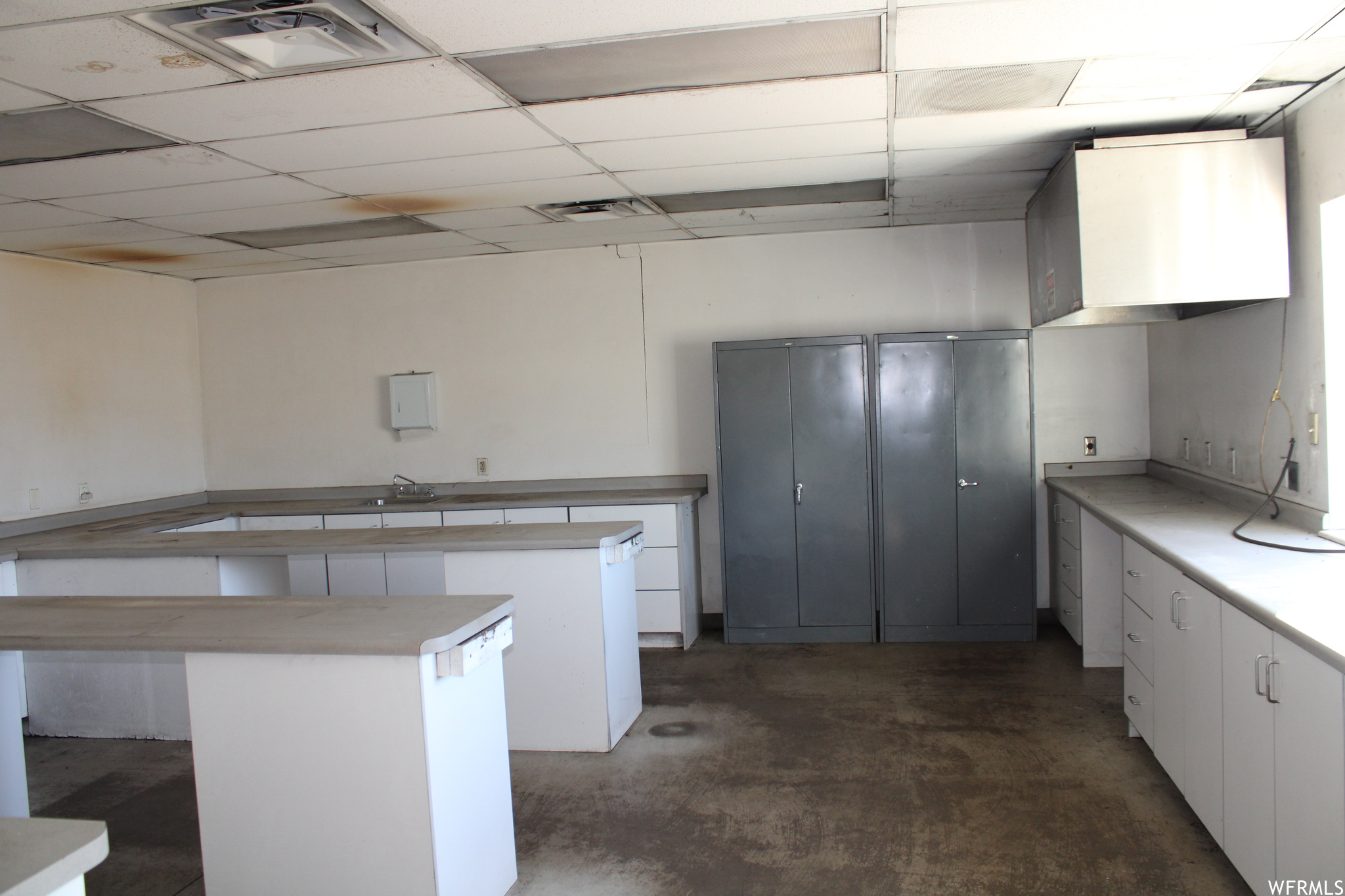 Room featuring a center island, a drop ceiling, and white cabinets