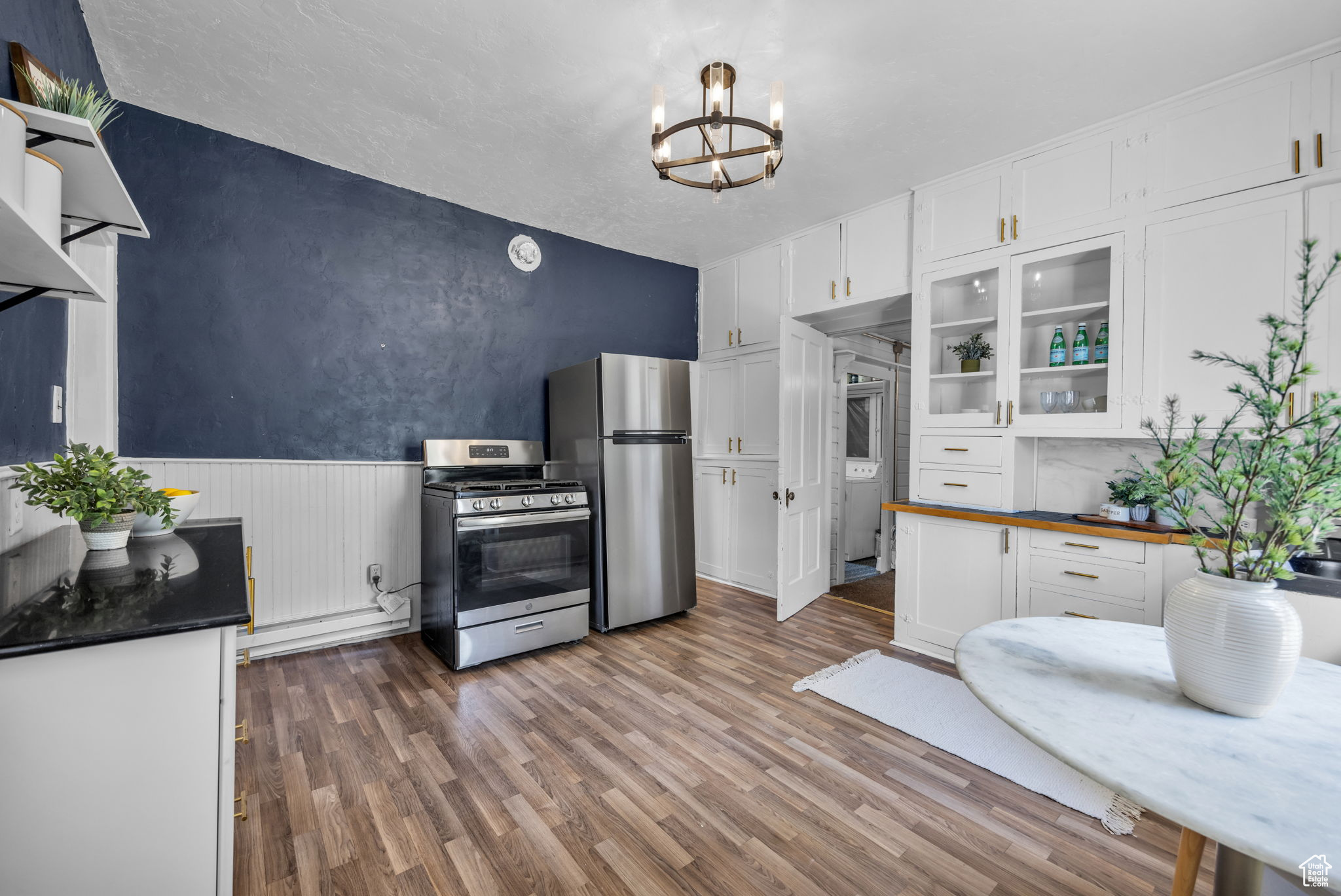 Kitchen featuring stainless steel appliances, pendant lighting, wood-style flooring, an inviting chandelier, and white cabinets