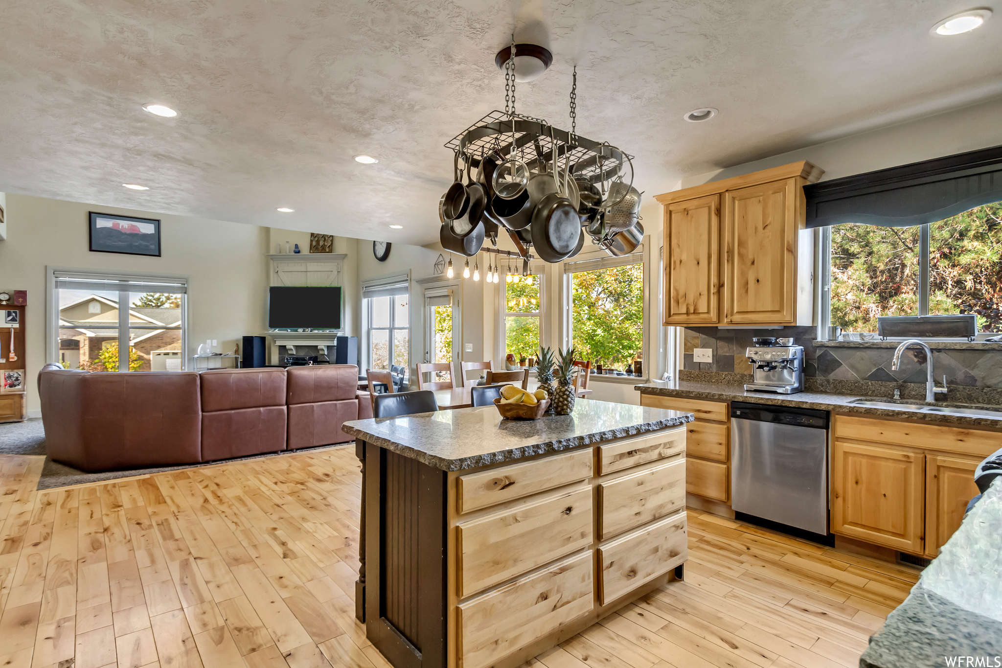 Kitchen with tasteful backsplash, light hardwood / wood-style flooring, sink, stainless steel dishwasher, and a notable chandelier