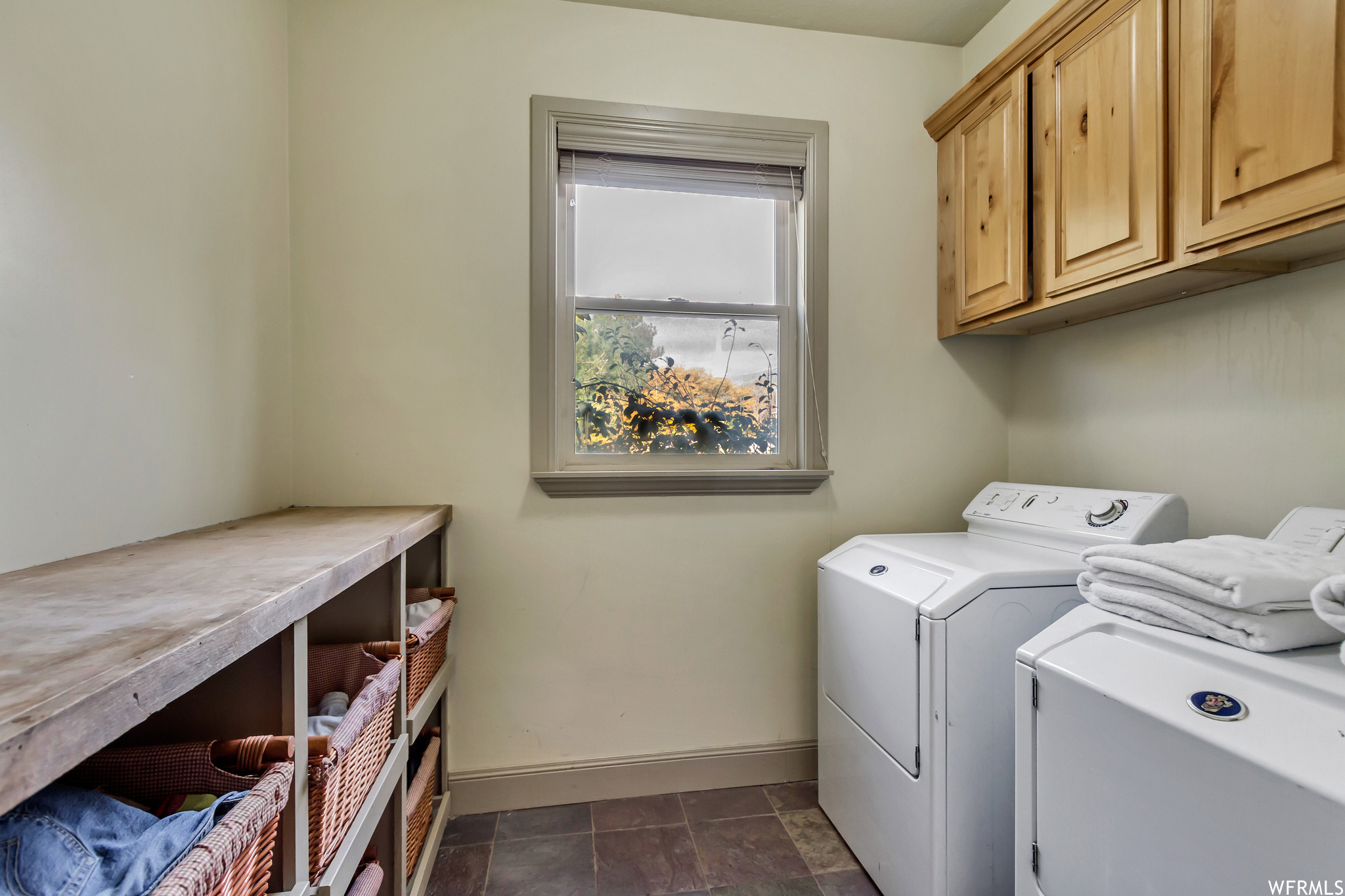 Laundry area featuring dark tile floors, washing machine and dryer, and cabinets