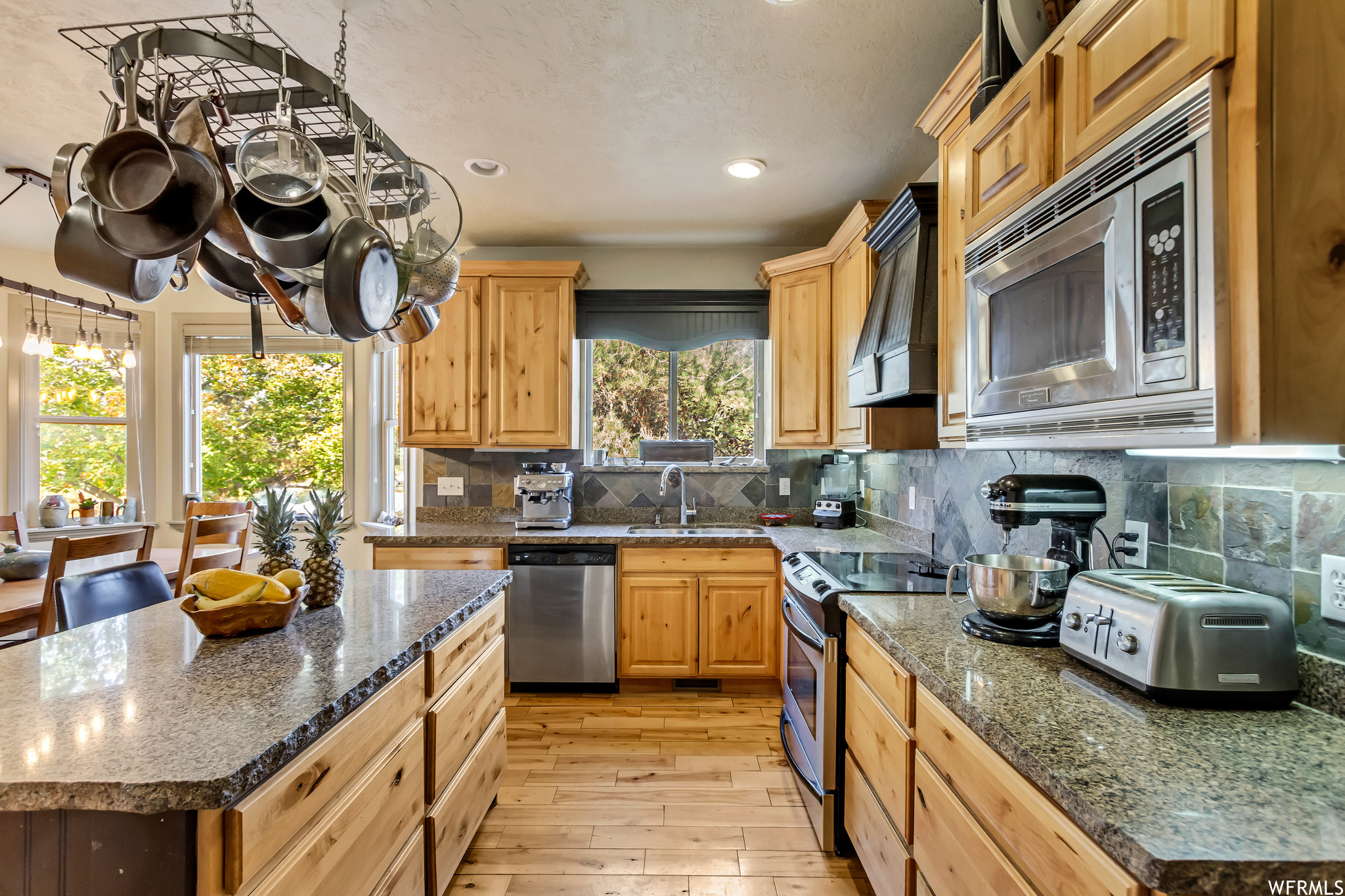 Kitchen with light hardwood / wood-style floors, backsplash, stainless steel appliances, and a kitchen island