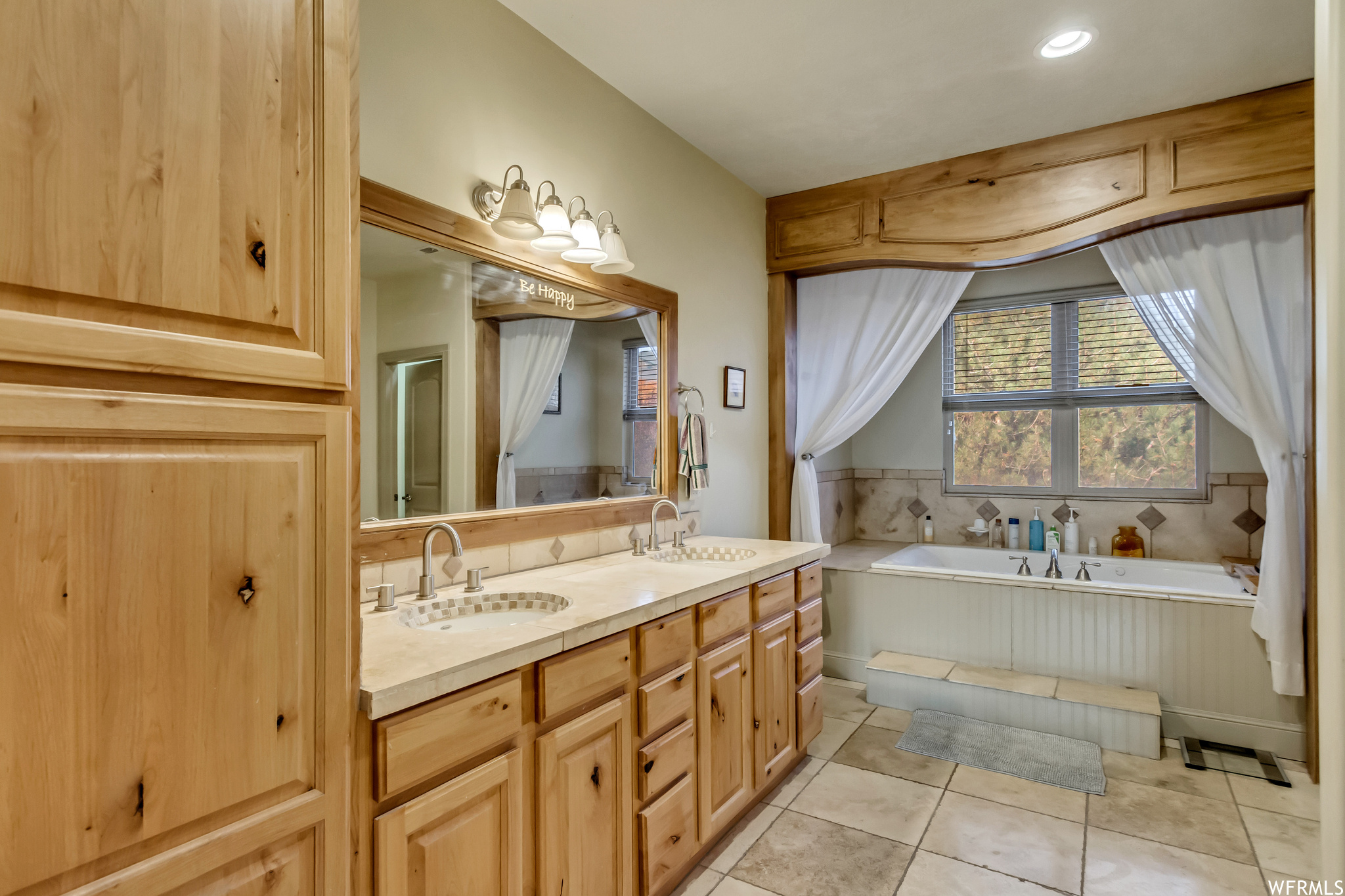 Bathroom featuring tile floors, dual sinks, a bath, and vanity with extensive cabinet space
