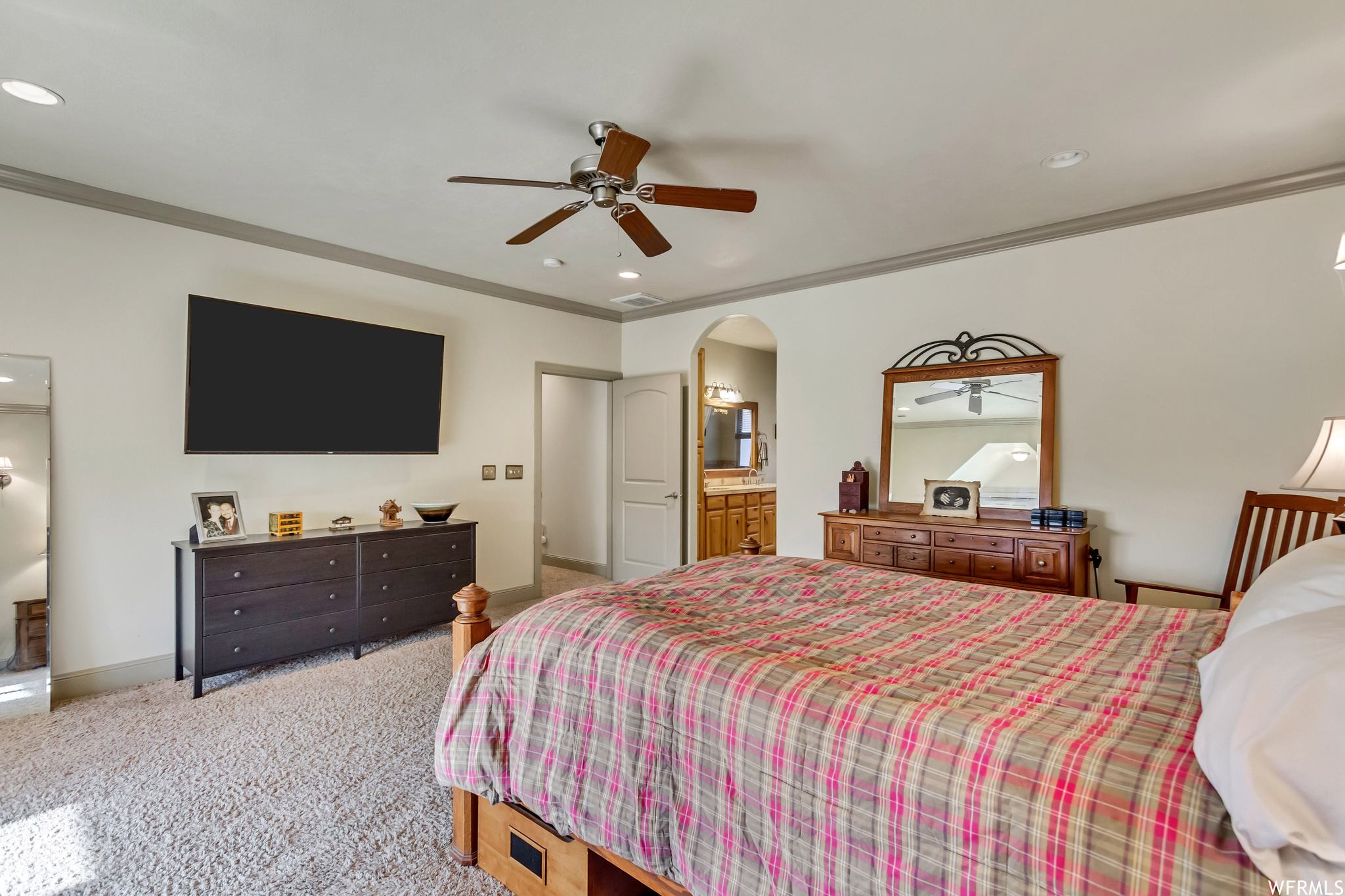 Carpeted bedroom featuring ceiling fan, ornamental molding, and ensuite bath