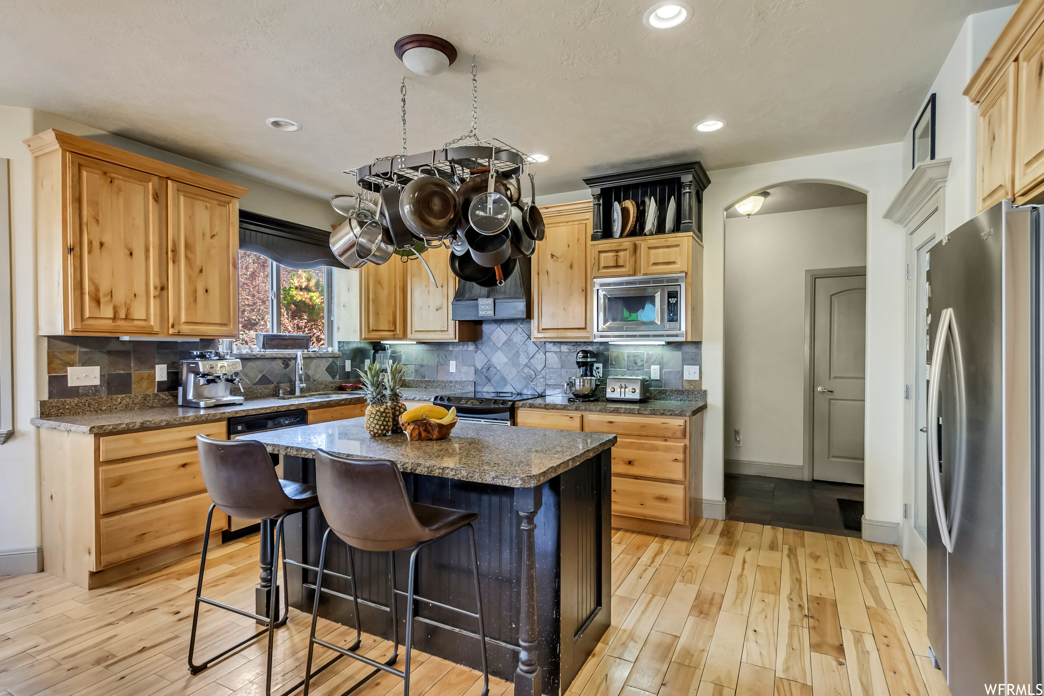 Kitchen featuring dark stone countertops, appliances with stainless steel finishes, a kitchen island, tasteful backsplash, and light wood-type flooring