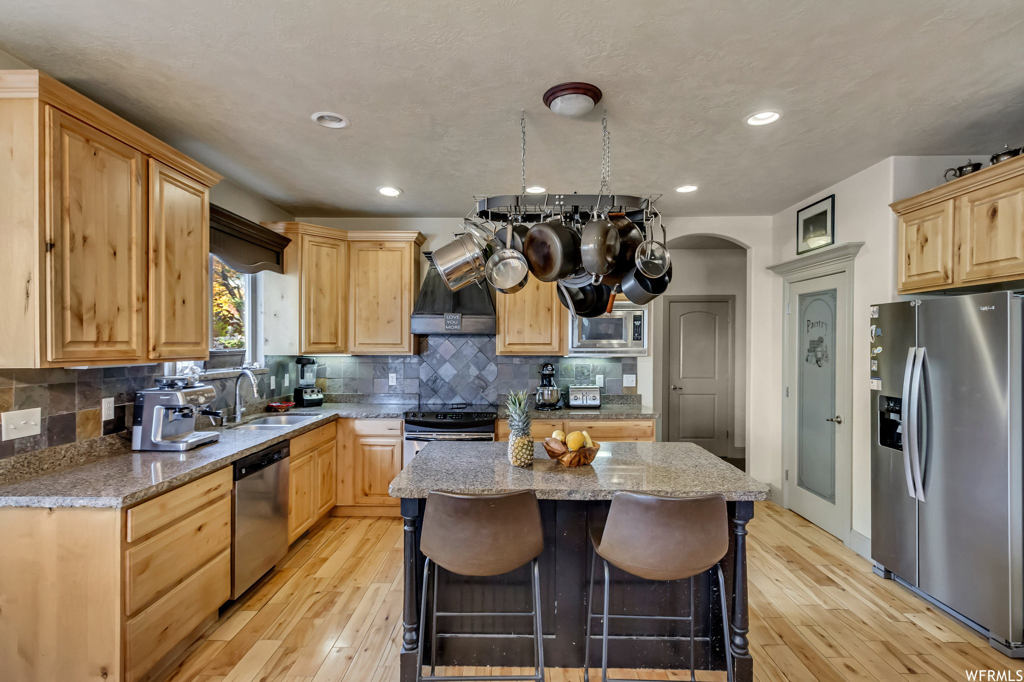 Kitchen featuring premium range hood, tasteful backsplash, light hardwood / wood-style flooring, a center island, and appliances with stainless steel finishes