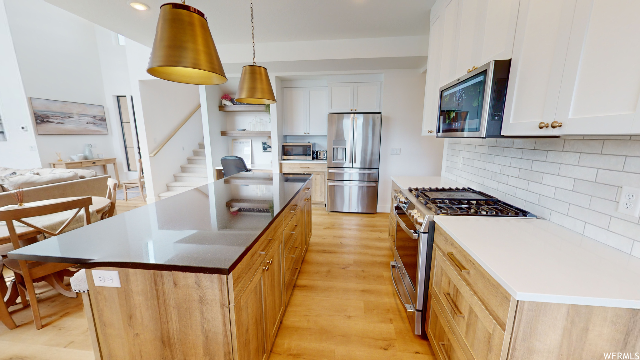 Kitchen featuring light hardwood / wood-style flooring, a center island, white cabinets, decorative light fixtures, and appliances with stainless steel finishes