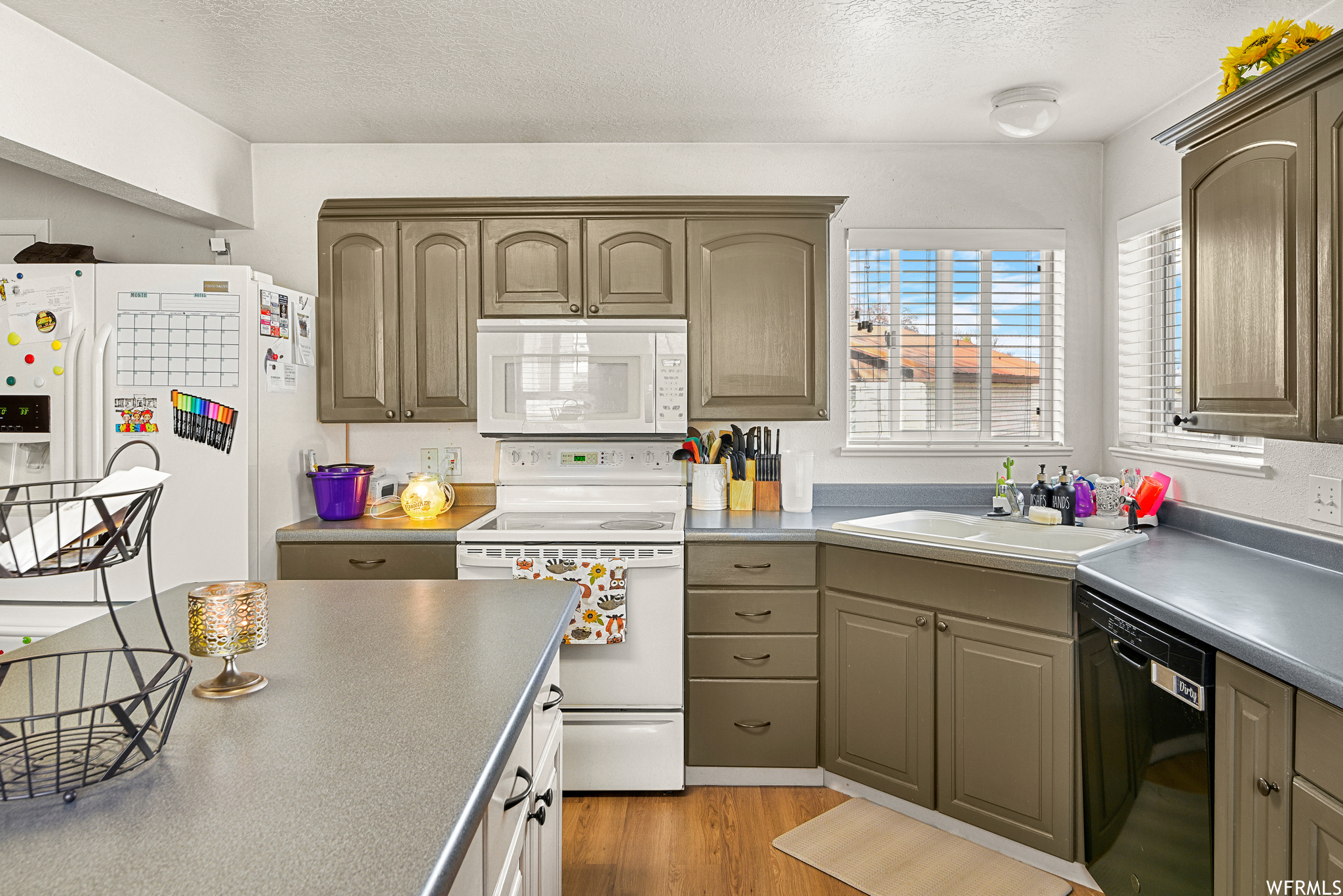 Kitchen featuring white appliances, light wood-type flooring, a textured ceiling, and sink