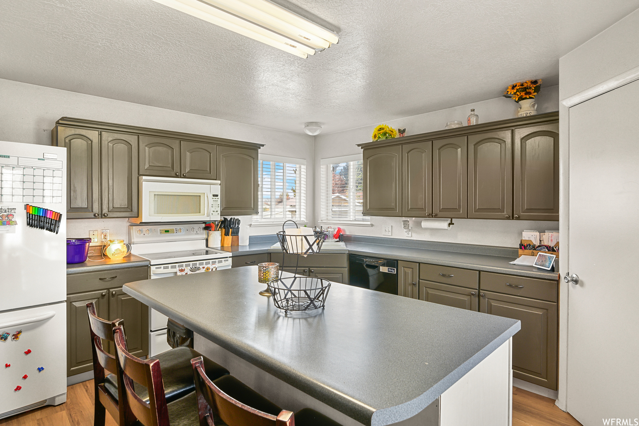 Kitchen featuring a kitchen bar, a kitchen island, a textured ceiling, light wood-type flooring, and white appliances