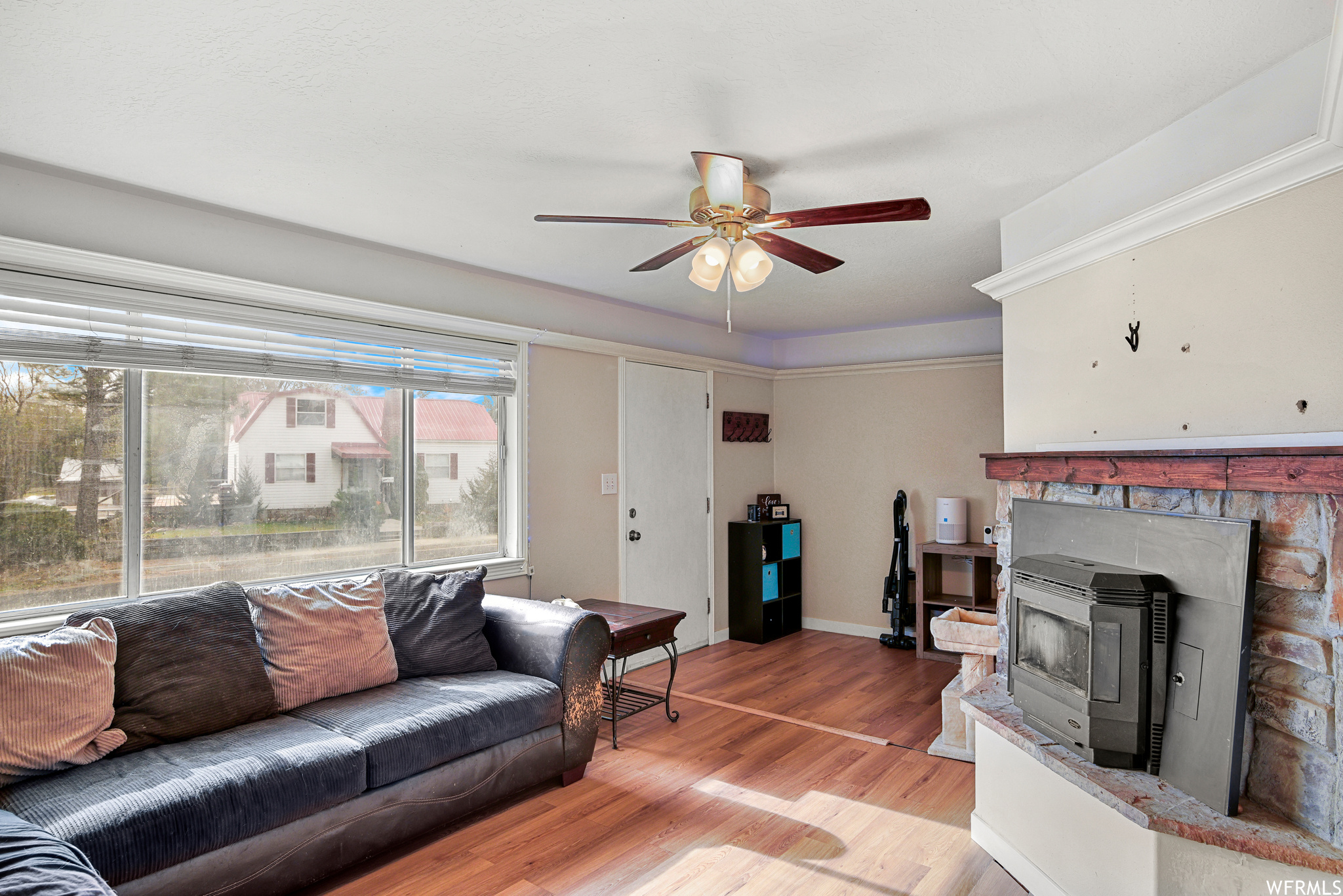 Living room with light wood-type flooring, a wood stove, and ceiling fan