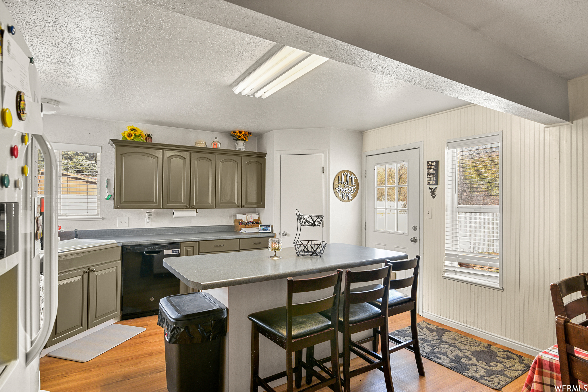 Kitchen with light hardwood / wood-style floors, a center island, dishwasher, sink, and a kitchen breakfast bar