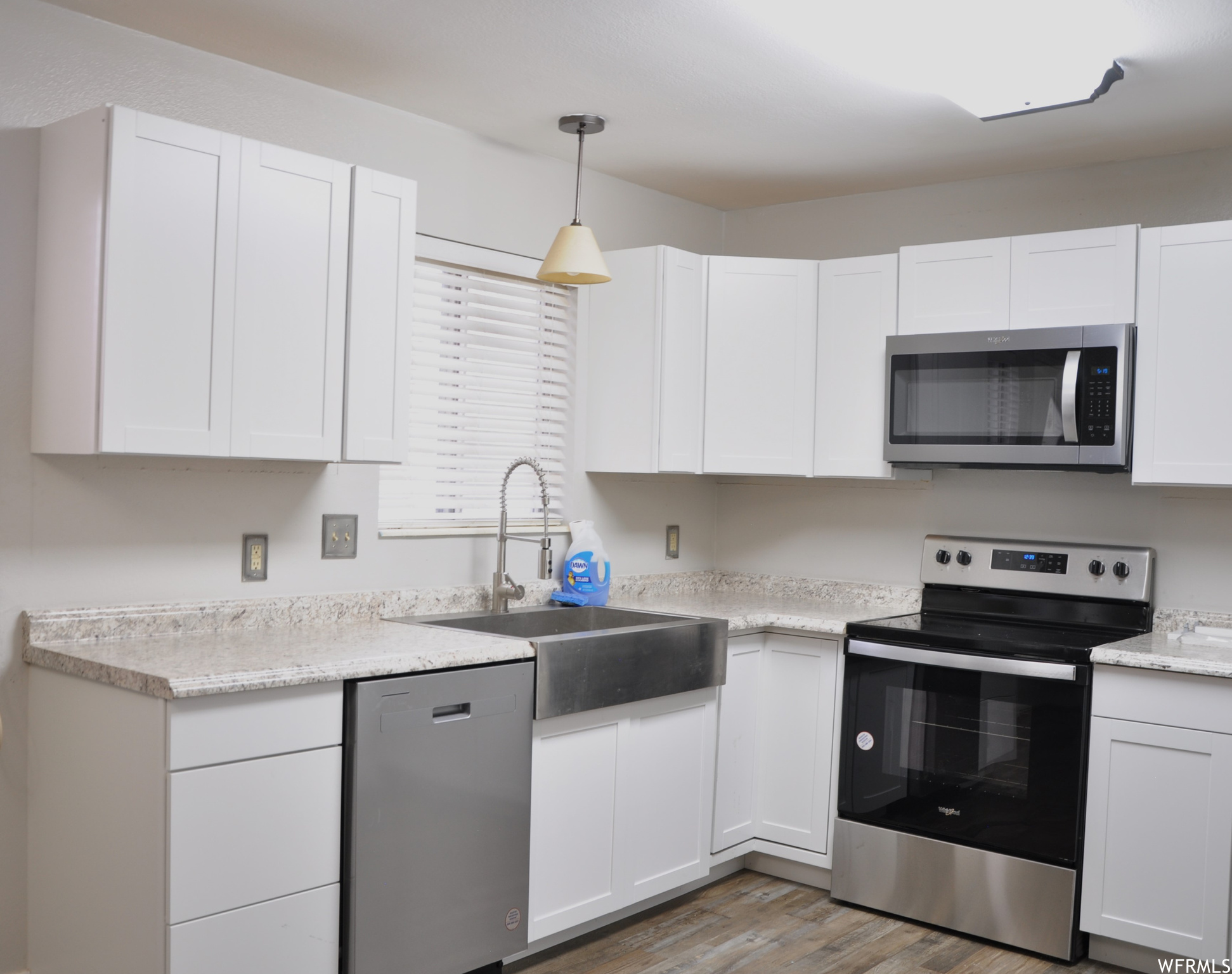 Kitchen featuring decorative light fixtures, wood-type flooring, appliances with stainless steel finishes, and white cabinetry