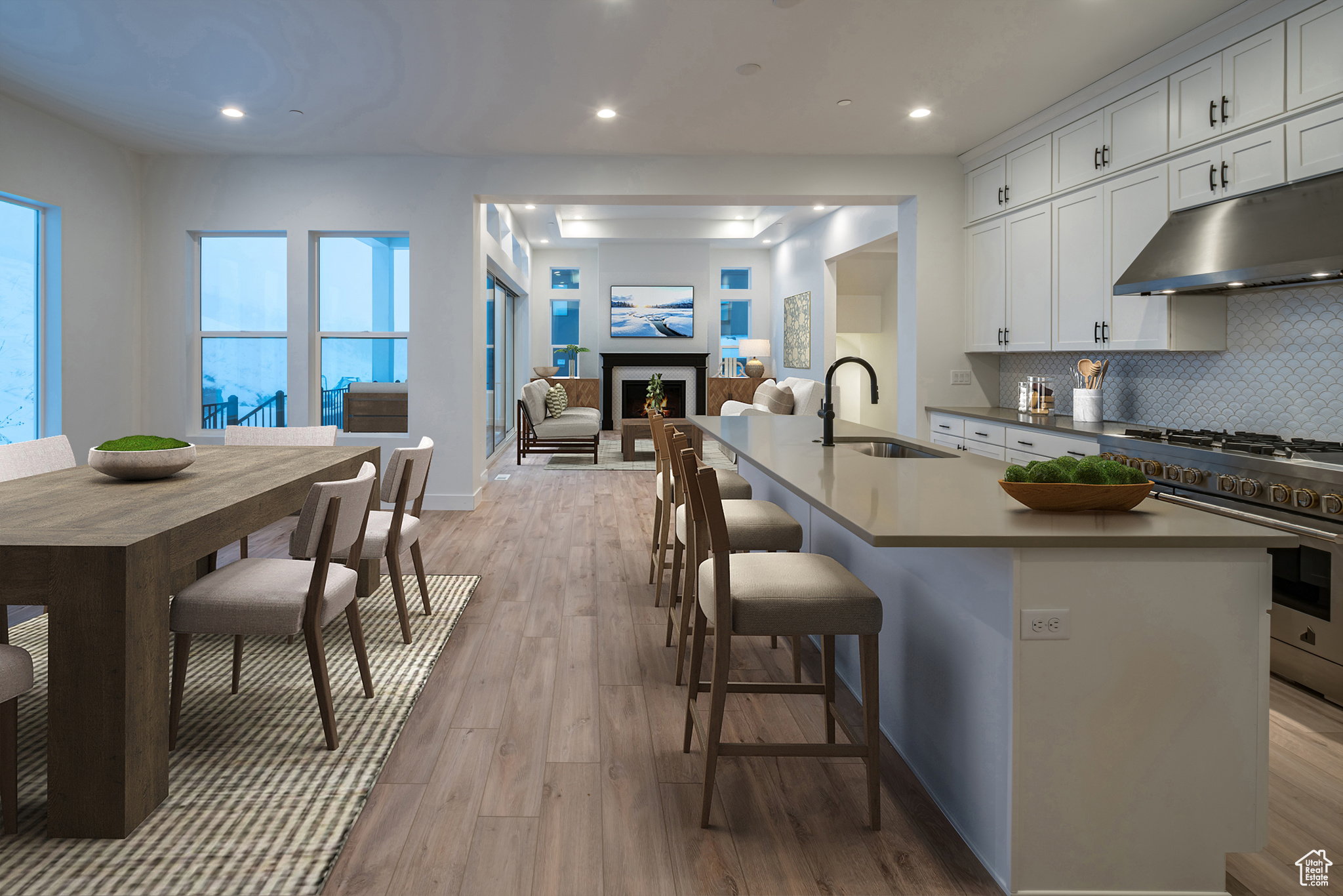 Kitchen featuring sink, light hardwood / wood-style floors, stainless steel stove, backsplash, and a center island with sink