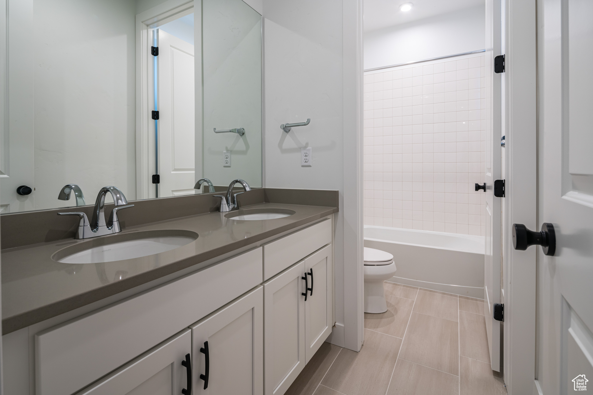 Full bathroom with double sink, toilet, large vanity,  shower combination, and tile flooring