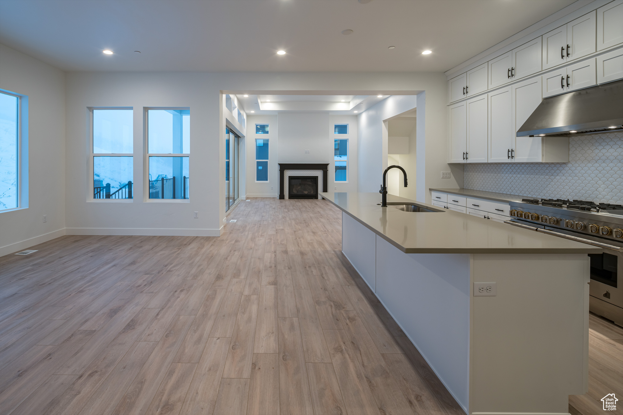 Kitchen with light hardwood / wood-style floors, stainless steel range, a kitchen island with sink, white cabinets, and sink