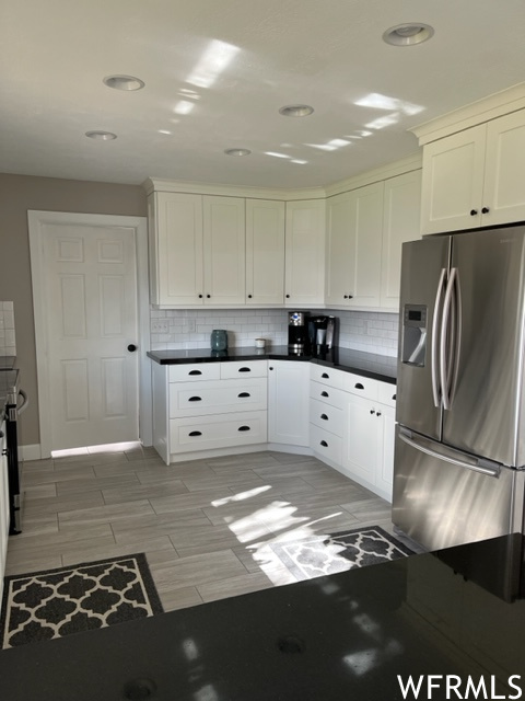 Kitchen with light tile floors, white cabinets, stainless steel fridge with ice dispenser, and tasteful backsplash
