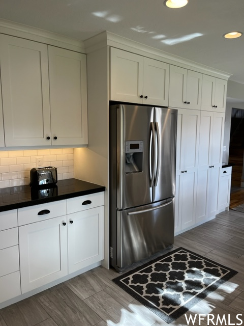 Kitchen with white cabinets, stainless steel refrigerator with ice dispenser, light hardwood / wood-style floors, and backsplash