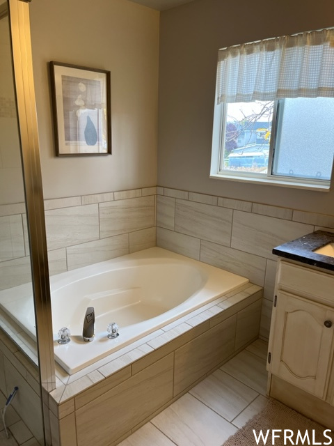Bathroom featuring tile floors, a relaxing tiled bath, and vanity