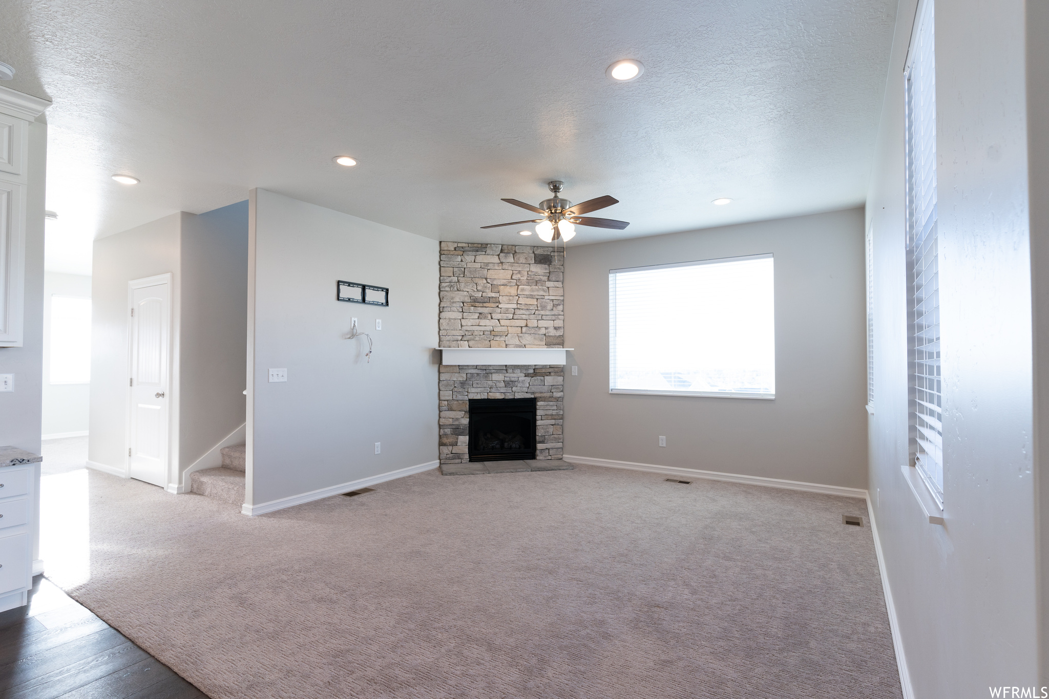 Unfurnished living room featuring a textured ceiling, ceiling fan, a fireplace, and light colored carpet