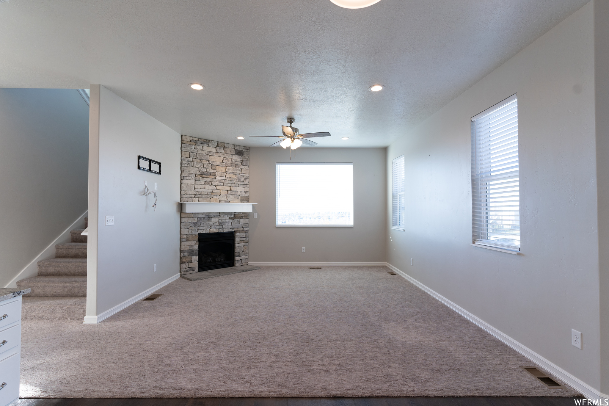Unfurnished living room featuring ceiling fan, a fireplace, plenty of natural light, and light carpet