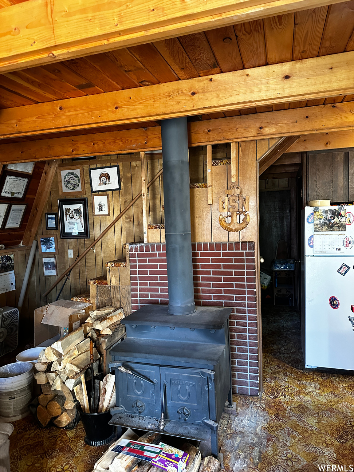 Room details with a wood stove, wooden walls, and white fridge