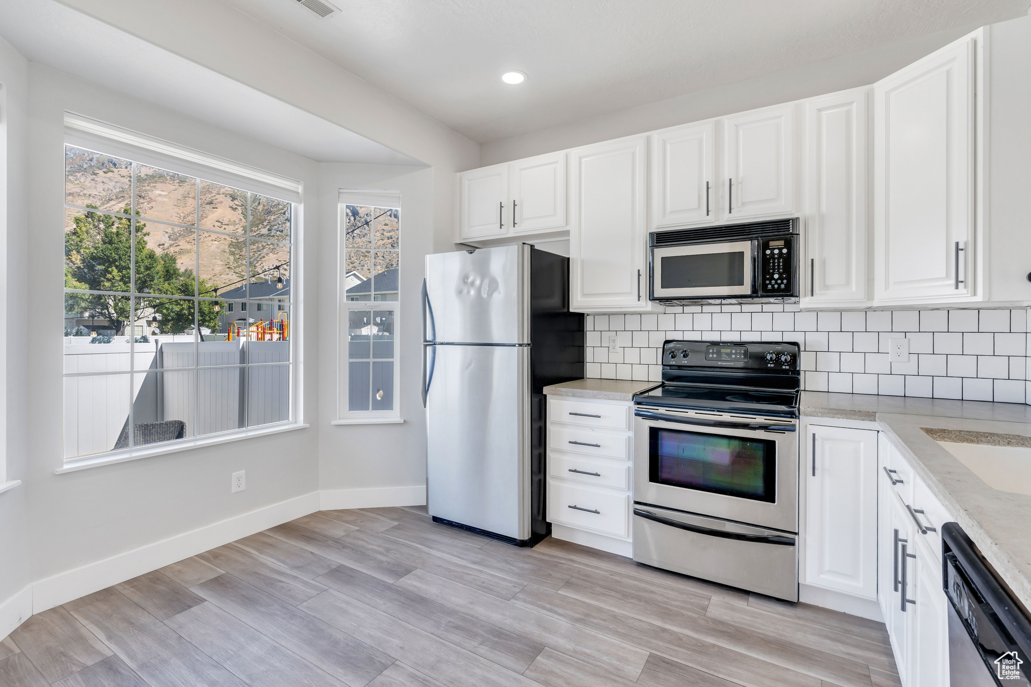 Kitchen with light hardwood / wood-style flooring, stainless steel appliances, backsplash, and white cabinetry