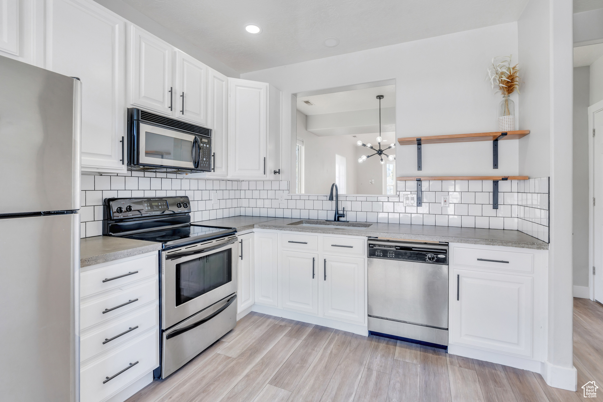 Kitchen with appliances with stainless steel finishes, white cabinetry, sink, and light hardwood / wood-style flooring