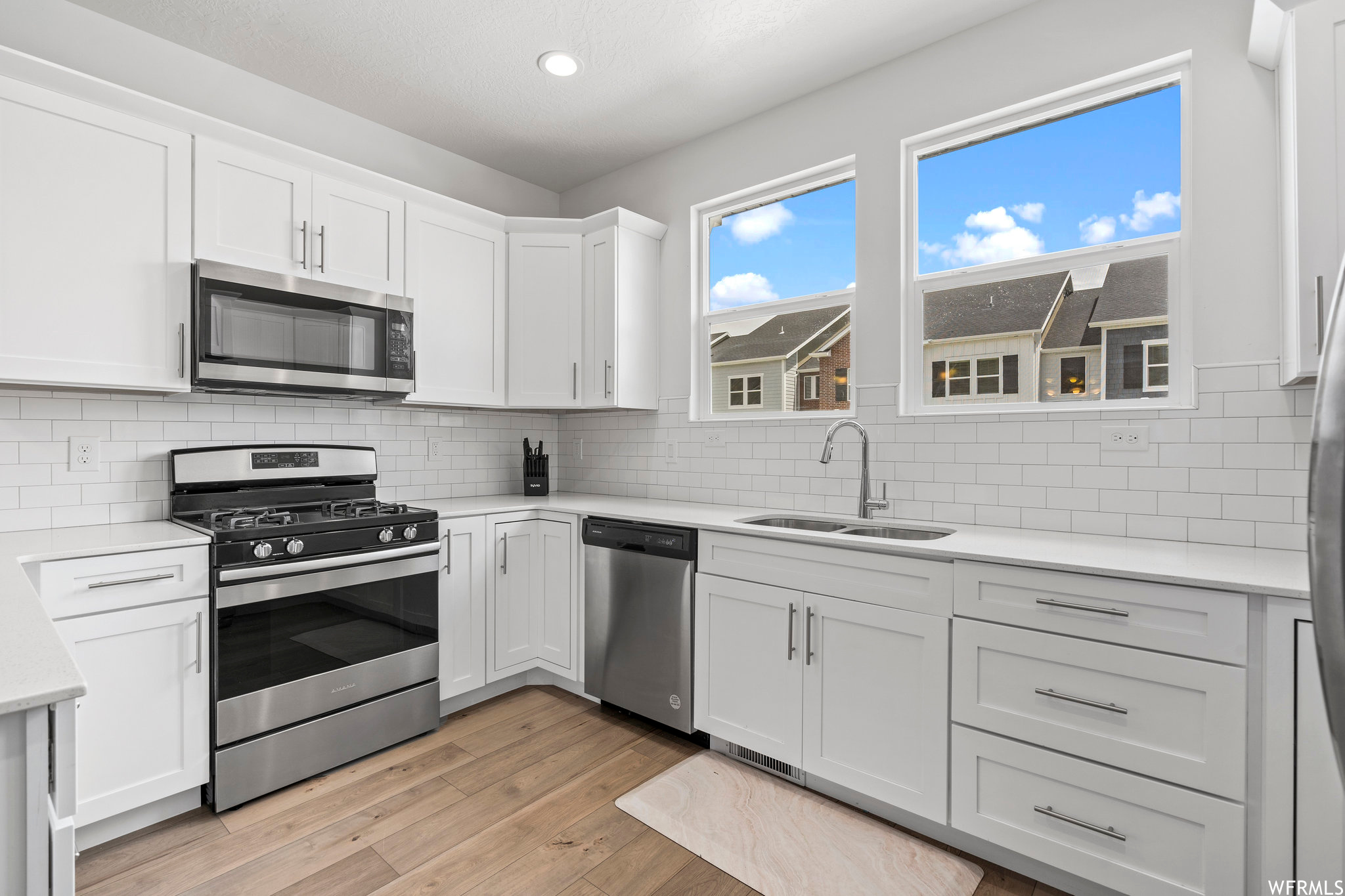 Kitchen with stainless steel appliances, backsplash, white cabinetry, and light hardwood / wood-style flooring