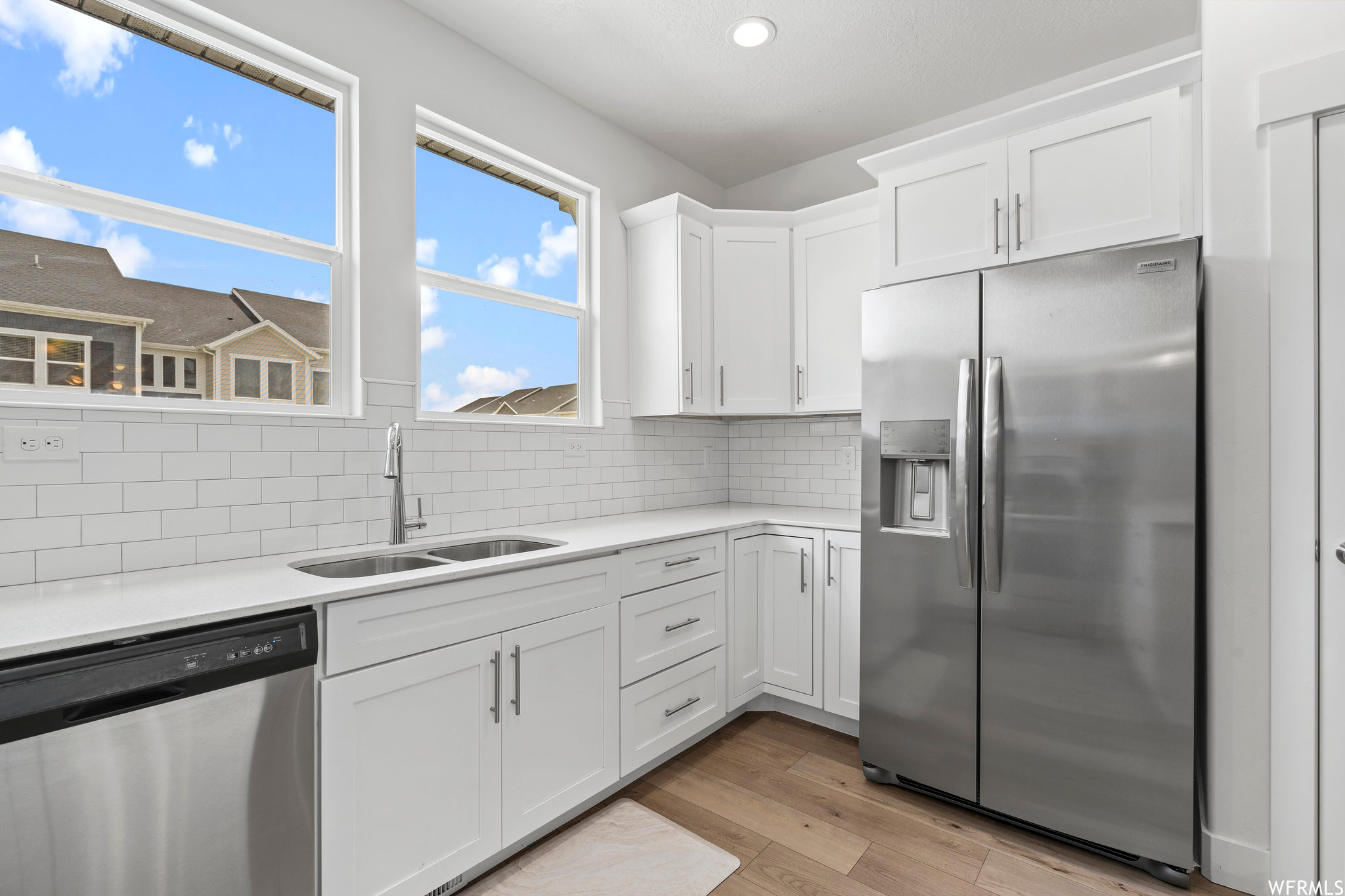 Kitchen with tasteful backsplash, sink, light hardwood / wood-style flooring, white cabinets, and appliances with stainless steel finishes