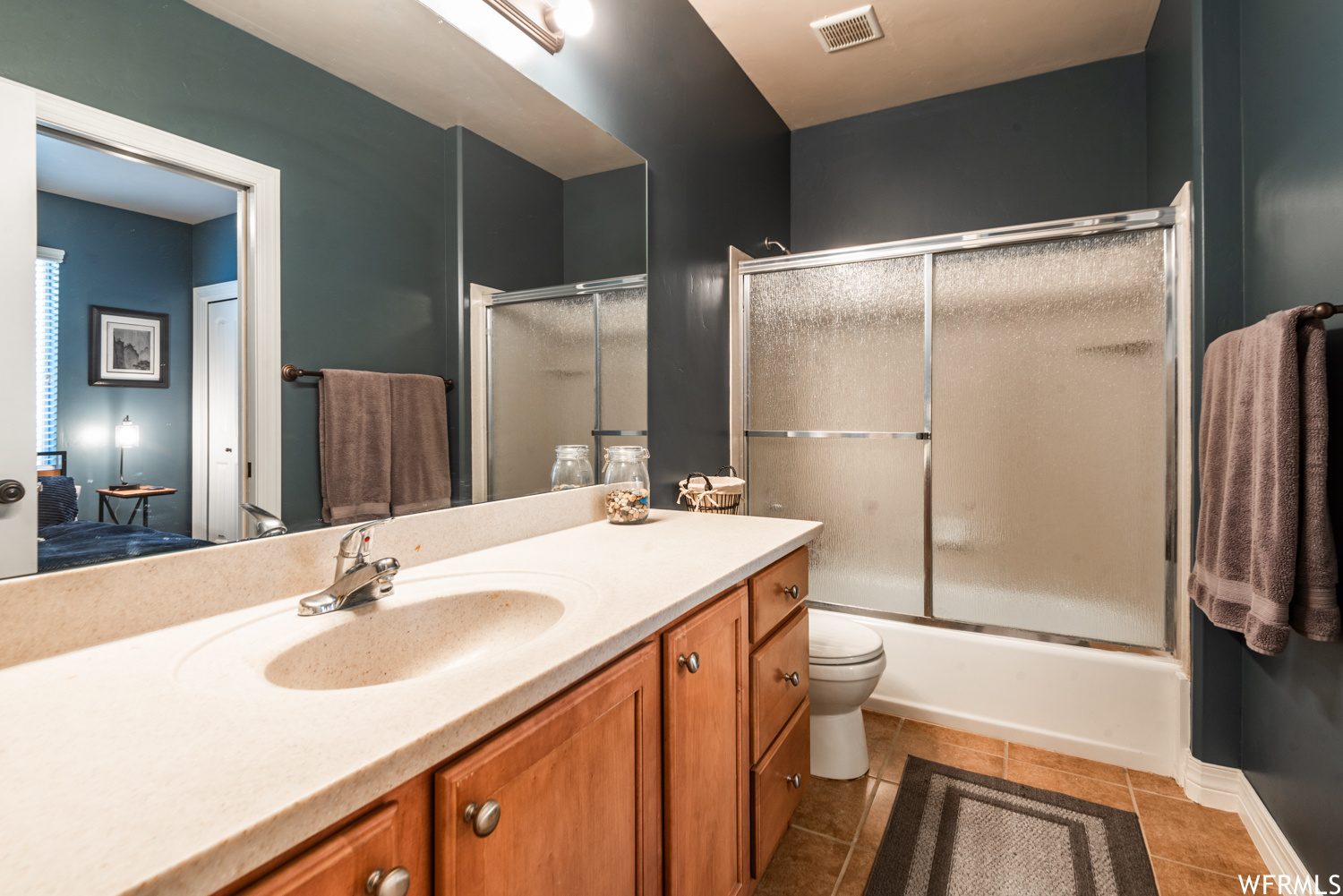 Full bathroom with toilet, combined bath / shower with glass door, tile floors, and large vanity