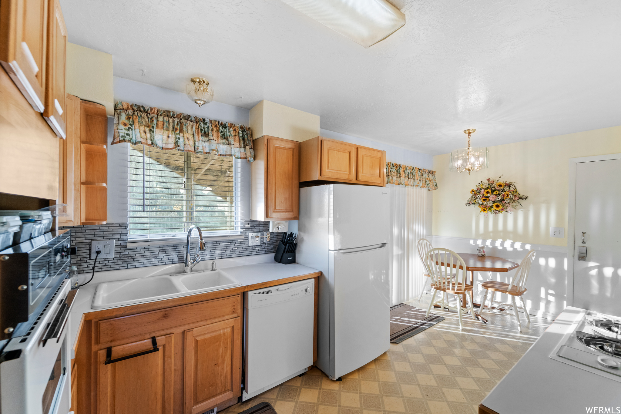 Kitchen with hanging light fixtures, sink, white appliances, backsplash, and light tile floors