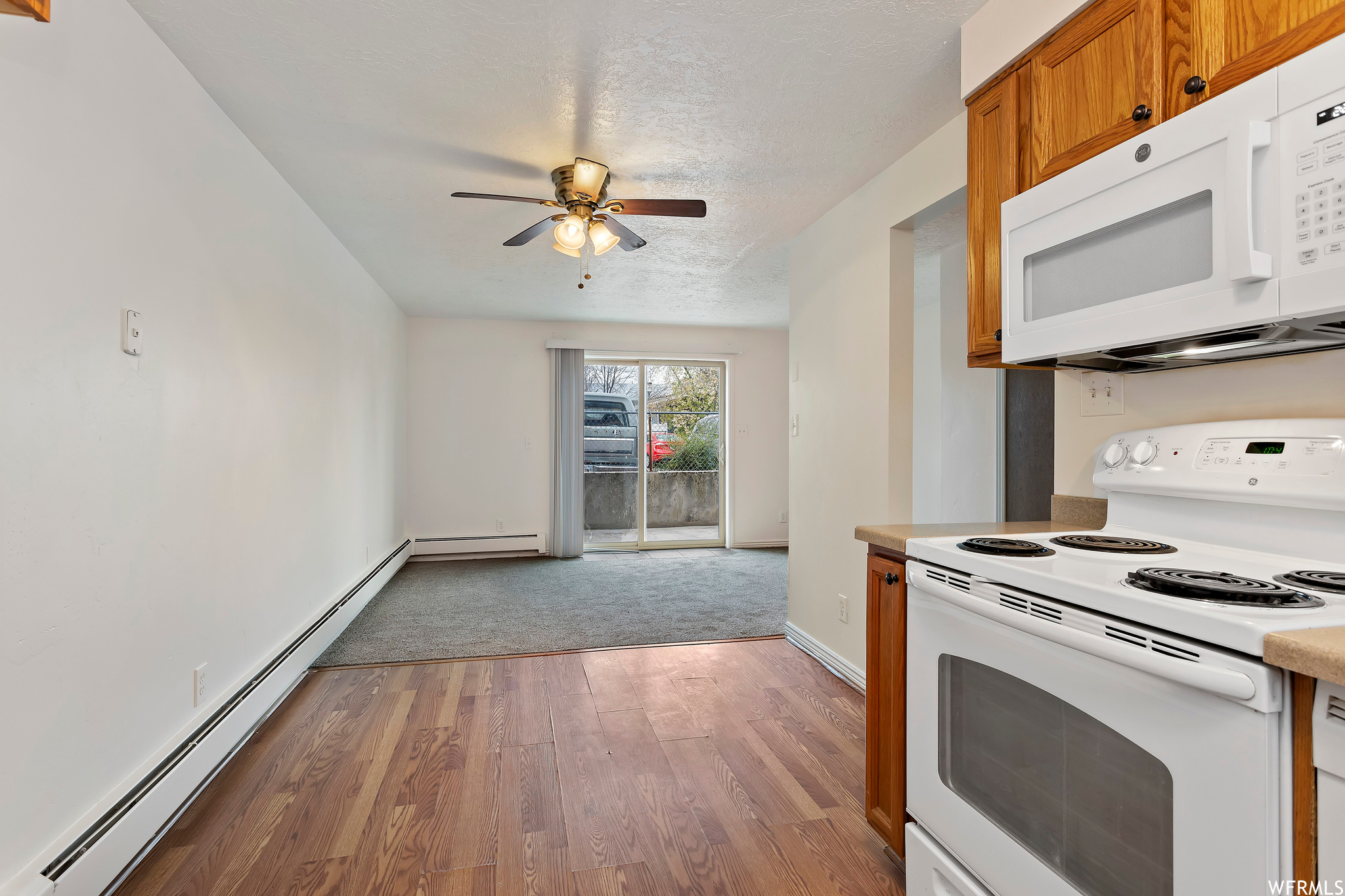 Kitchen featuring white appliances, ceiling fan, a baseboard radiator, and wood-type flooring