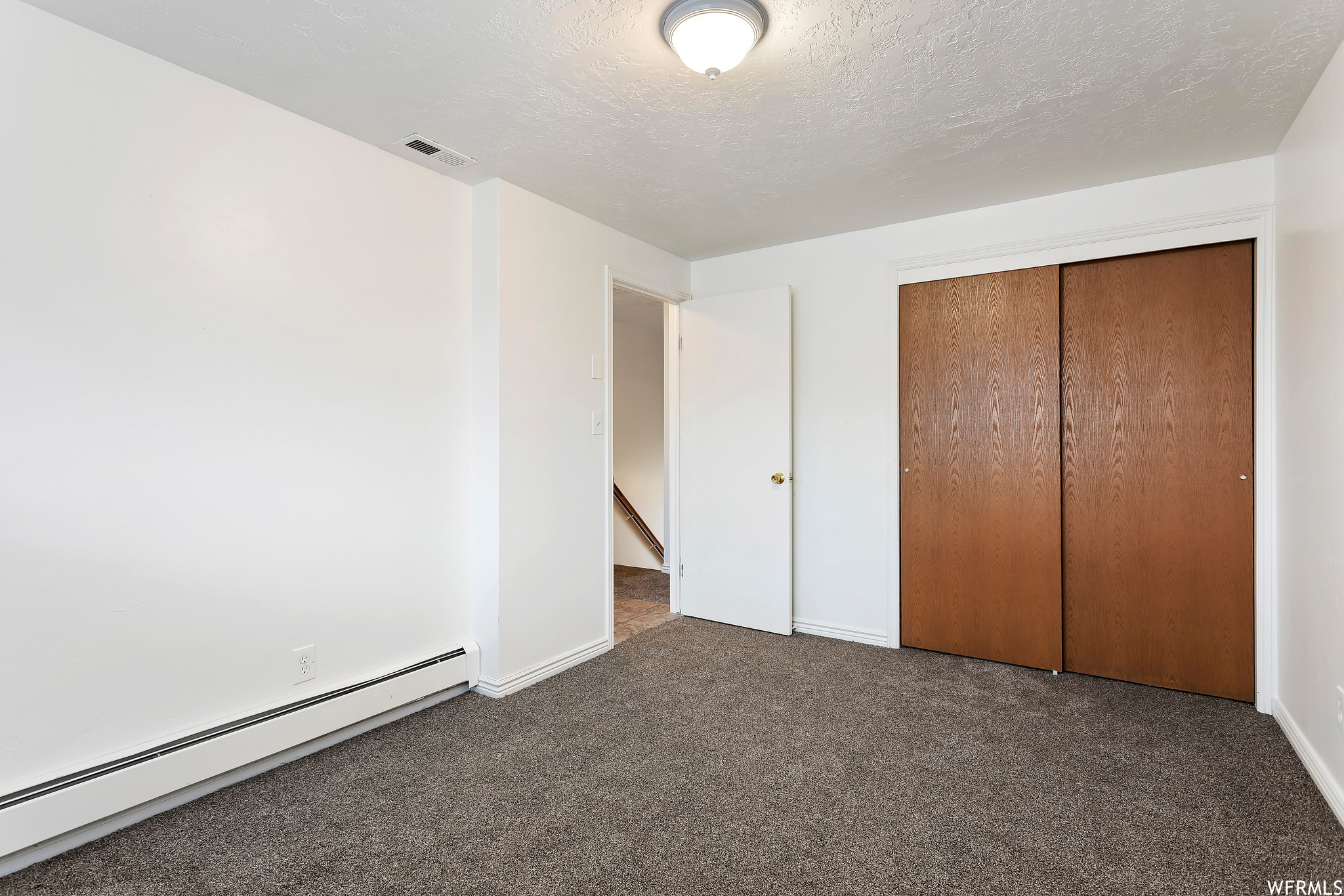 Unfurnished bedroom with dark carpet, a closet, baseboard heating, and a textured ceiling