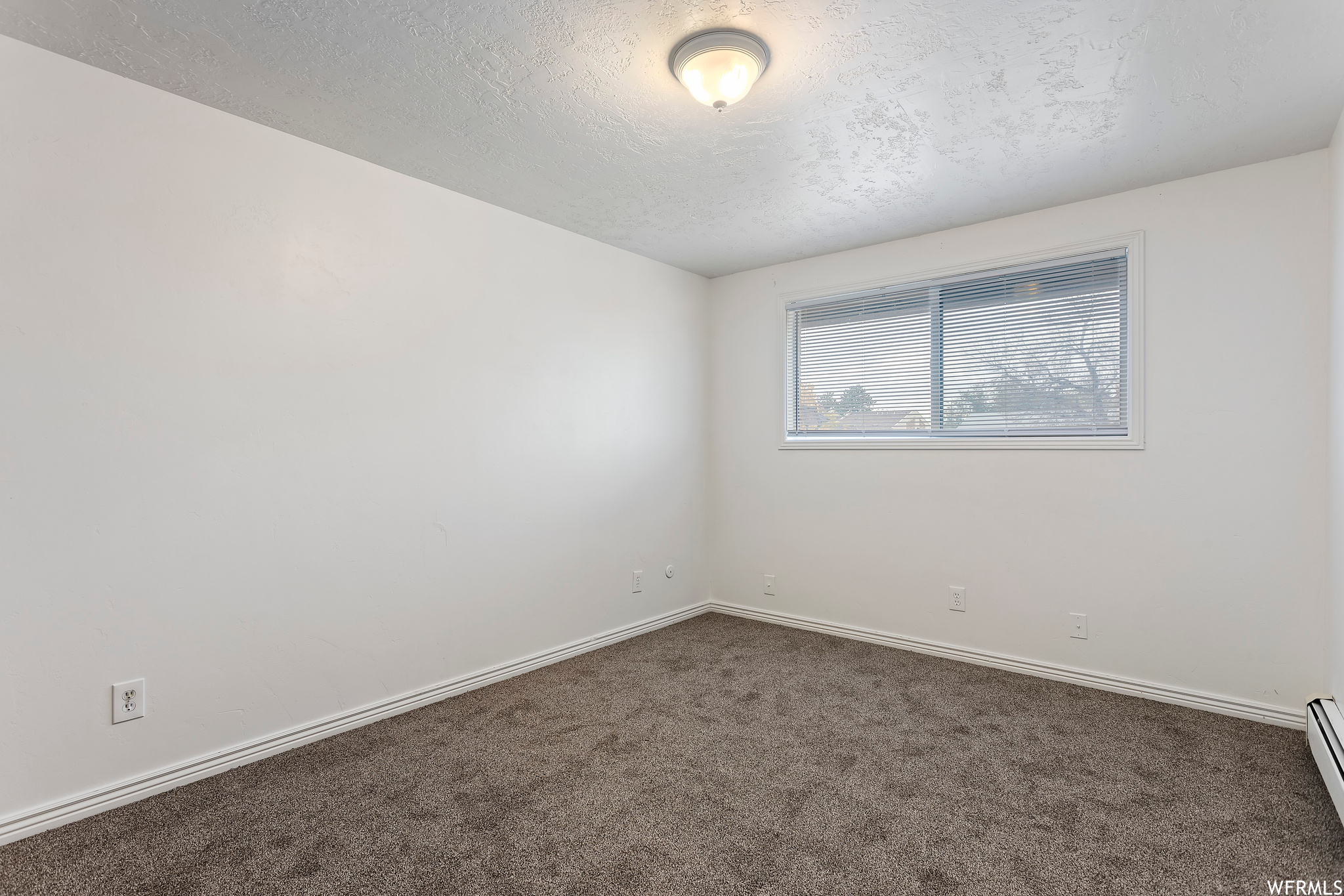 Spare room with dark colored carpet, a textured ceiling, and a baseboard heating unit