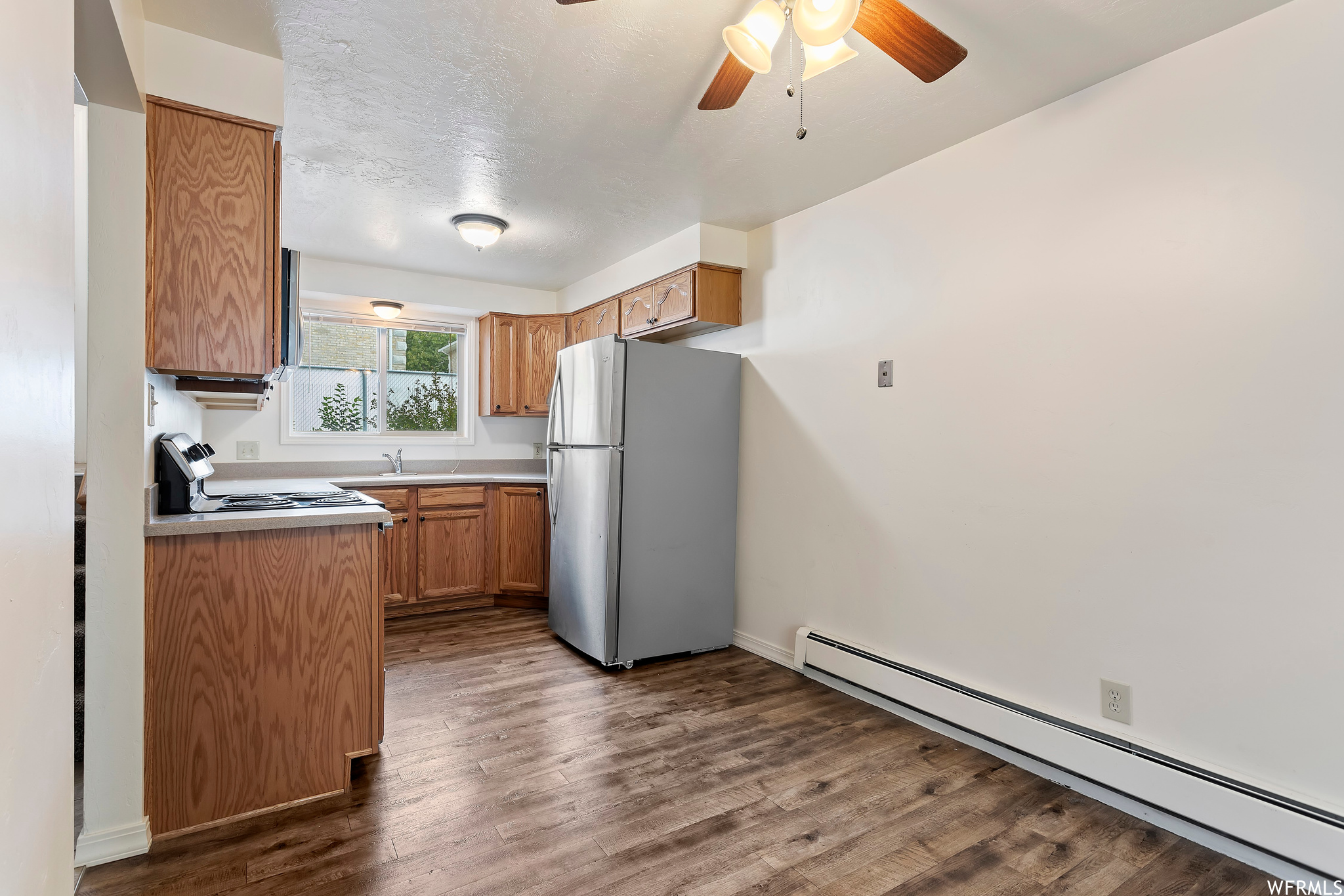 Kitchen featuring a baseboard heating unit, range, ceiling fan, stainless steel fridge, and dark hardwood / wood-style floors