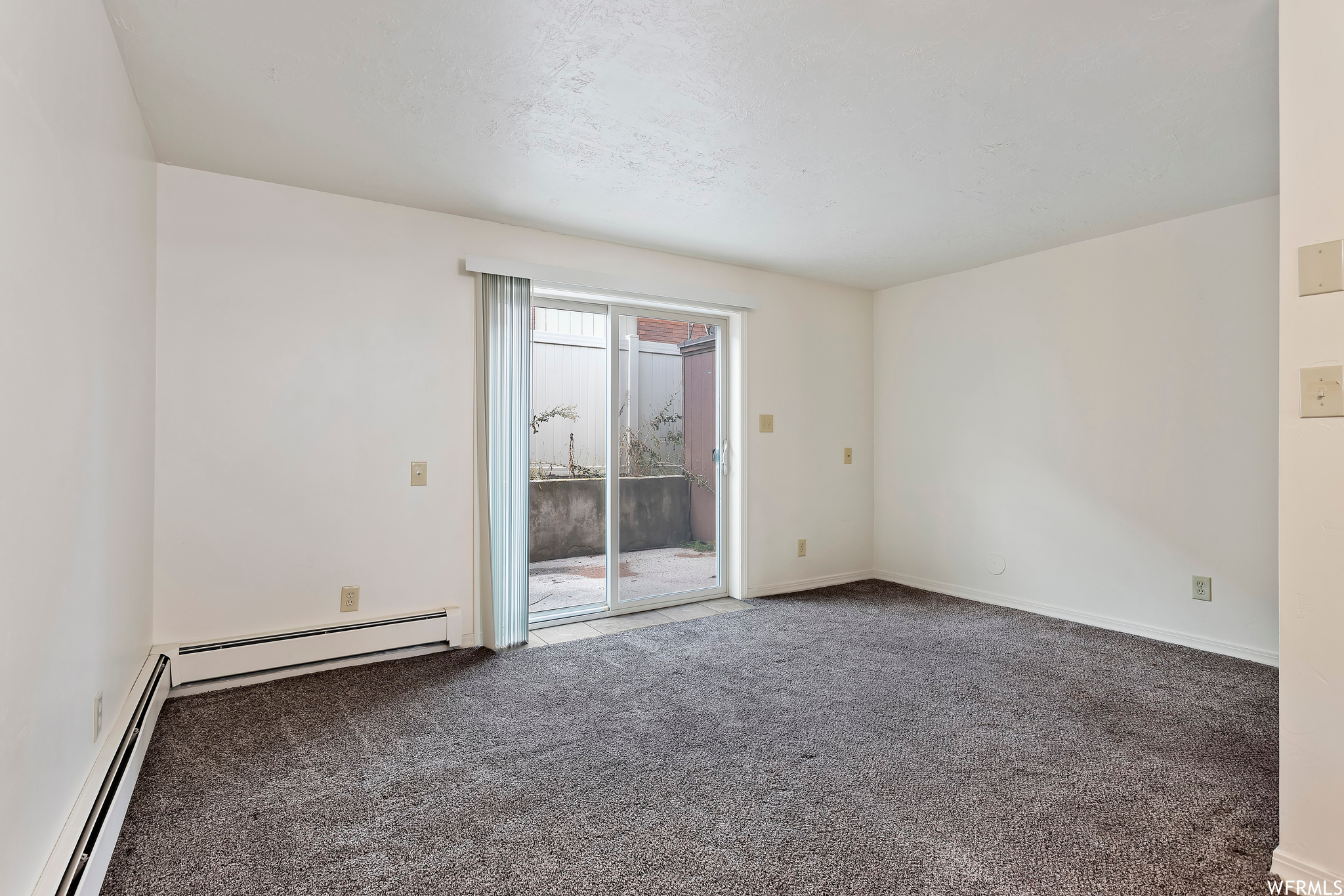 Empty room with dark colored carpet, baseboard heating, and a healthy amount of sunlight
