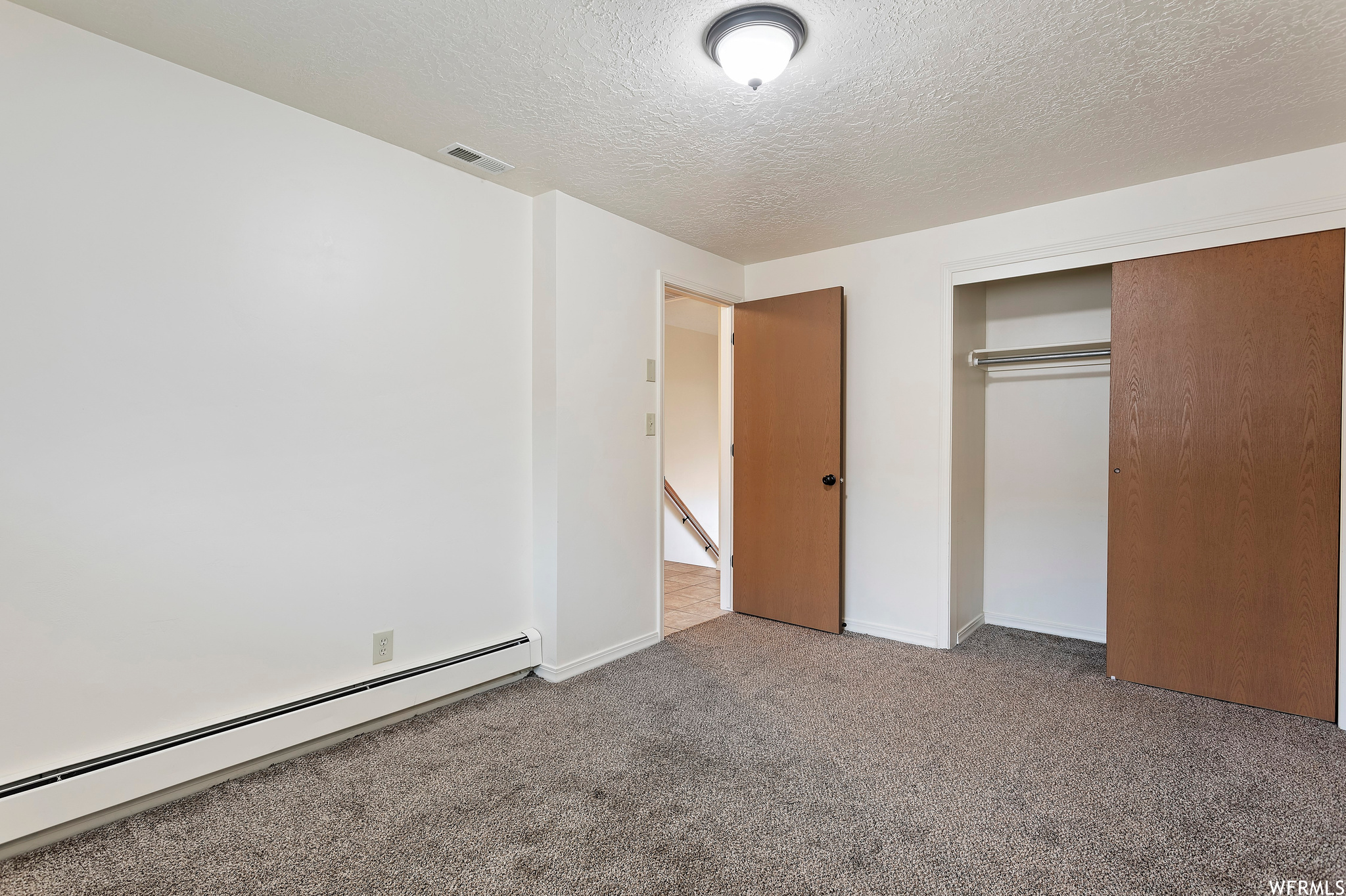 Unfurnished bedroom featuring a closet, baseboard heating, and carpet