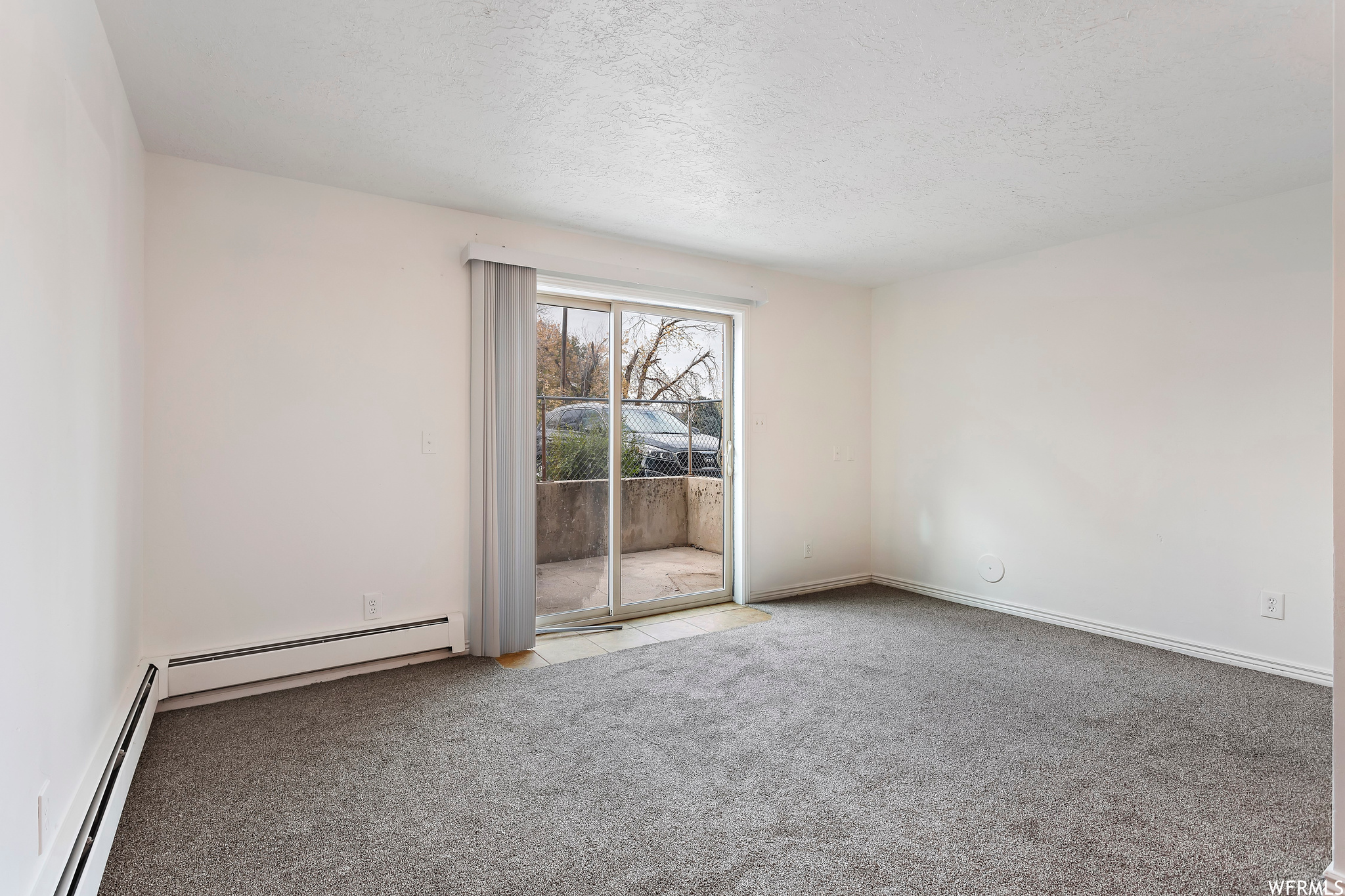 Carpeted spare room with a textured ceiling and a baseboard heating unit