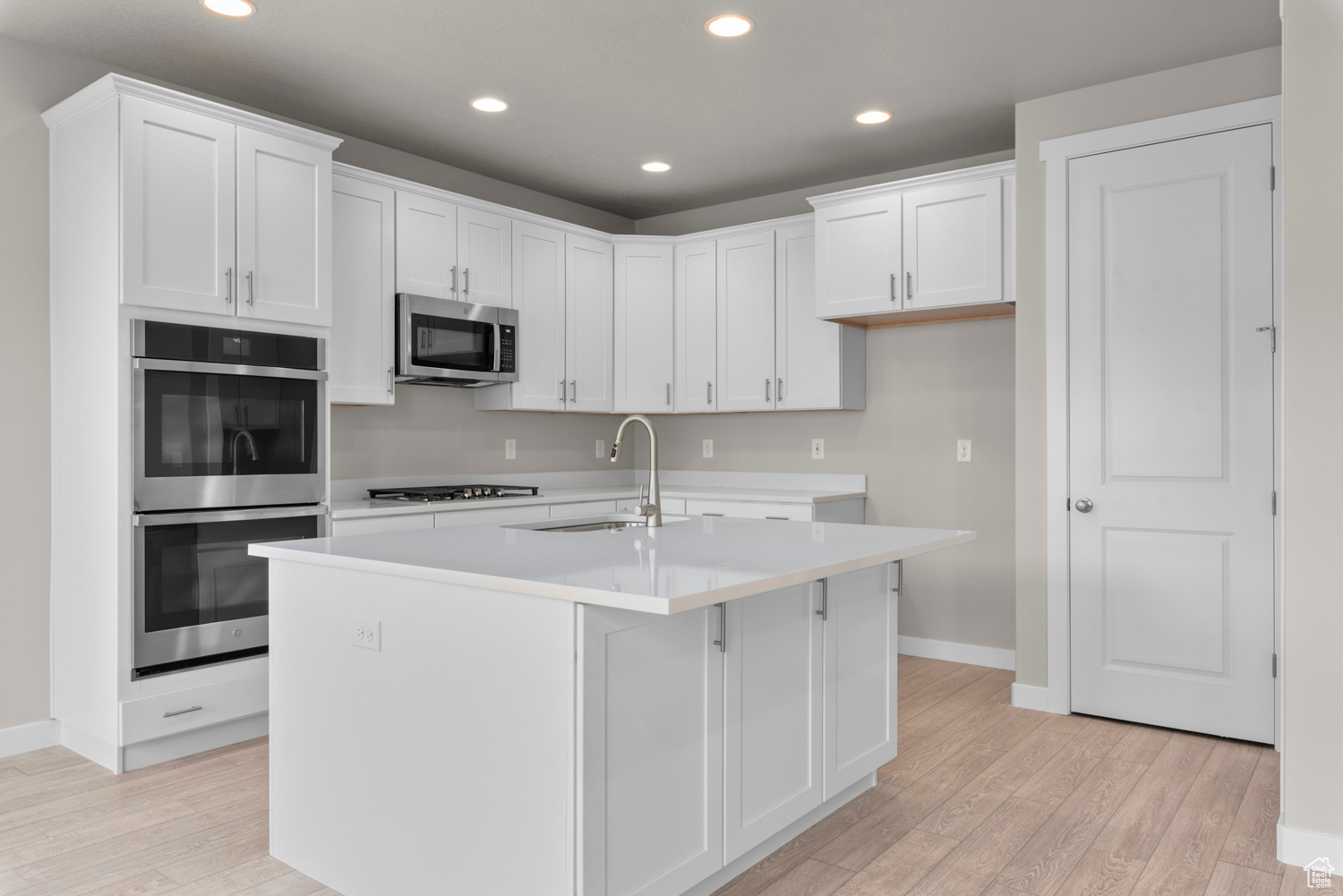 Kitchen with a kitchen island with sink, white cabinetry, sink, appliances with stainless steel finishes, and light hardwood / wood-style flooring