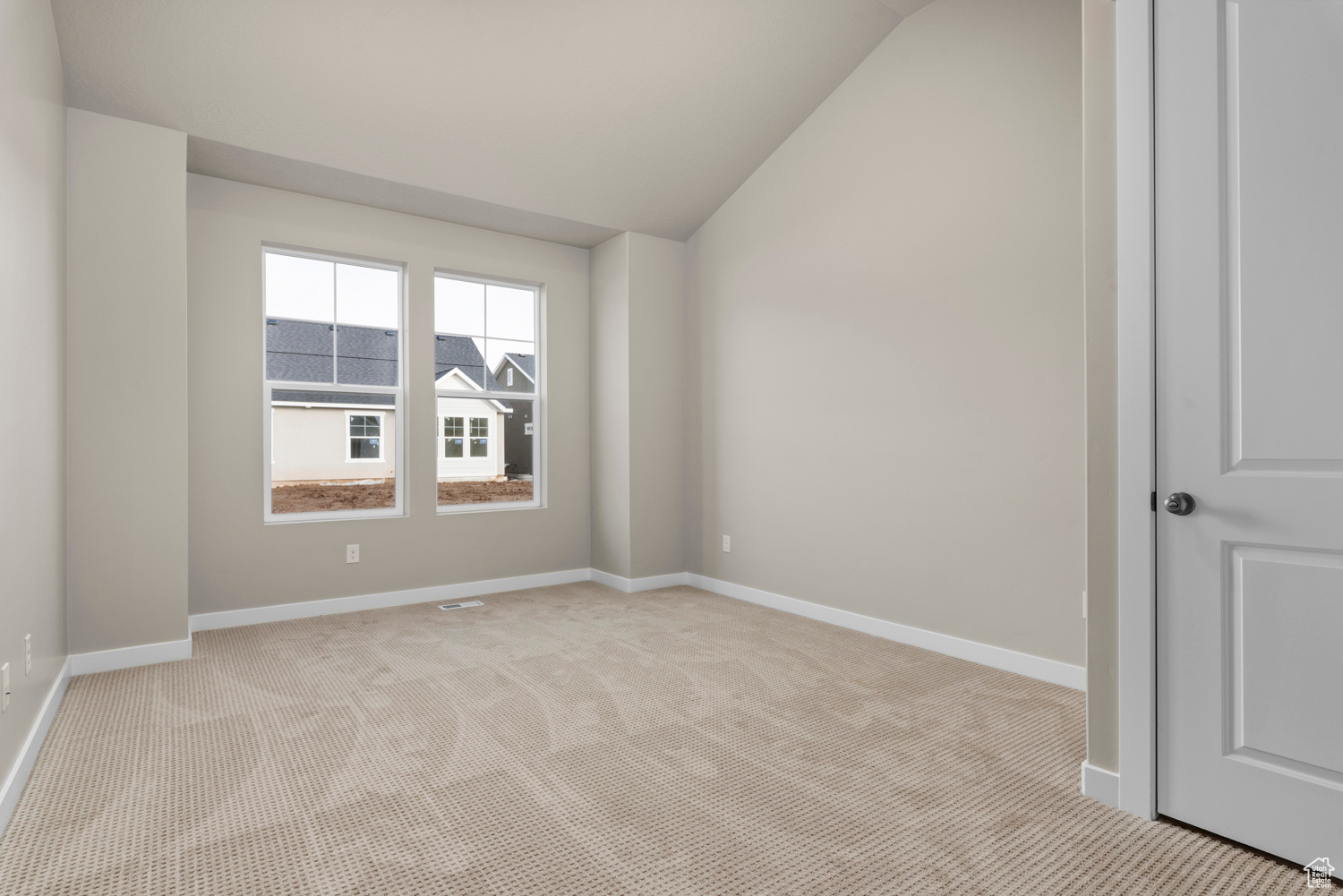 Empty room with light colored carpet and vaulted ceiling