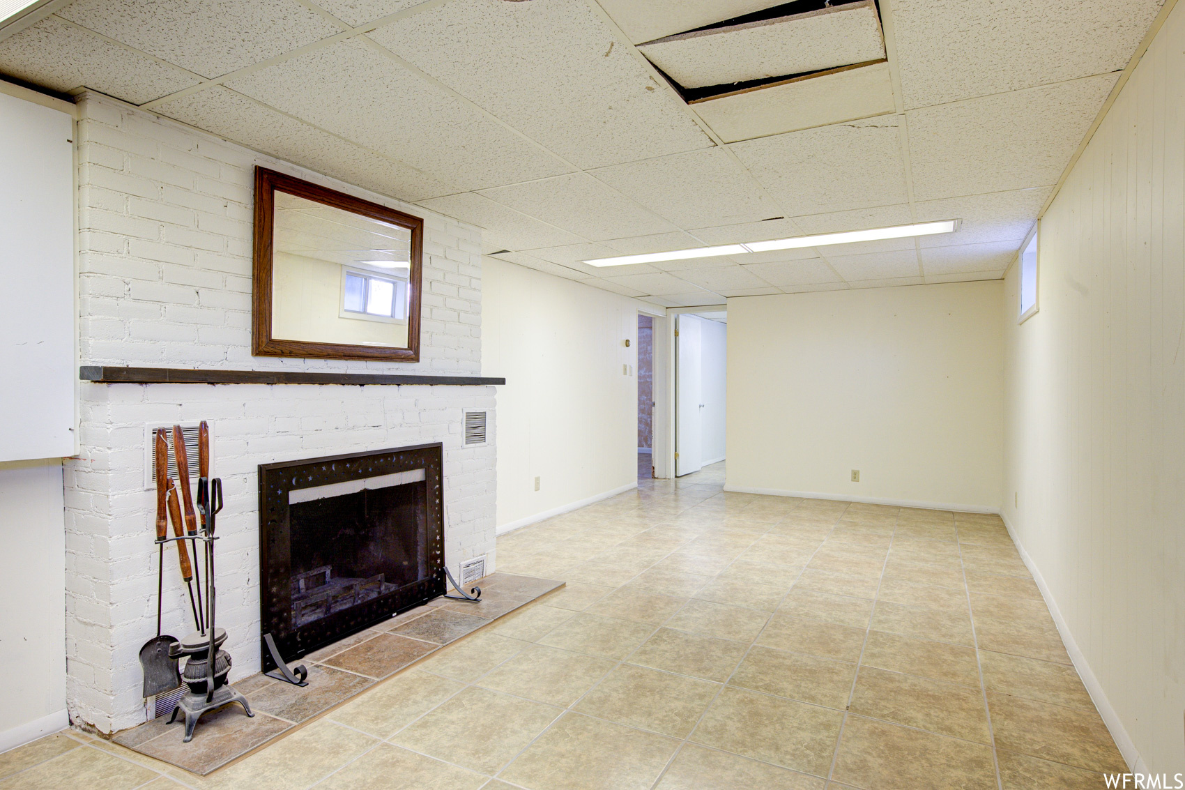 Unfurnished living room with a drop ceiling, a fireplace, and brick wall