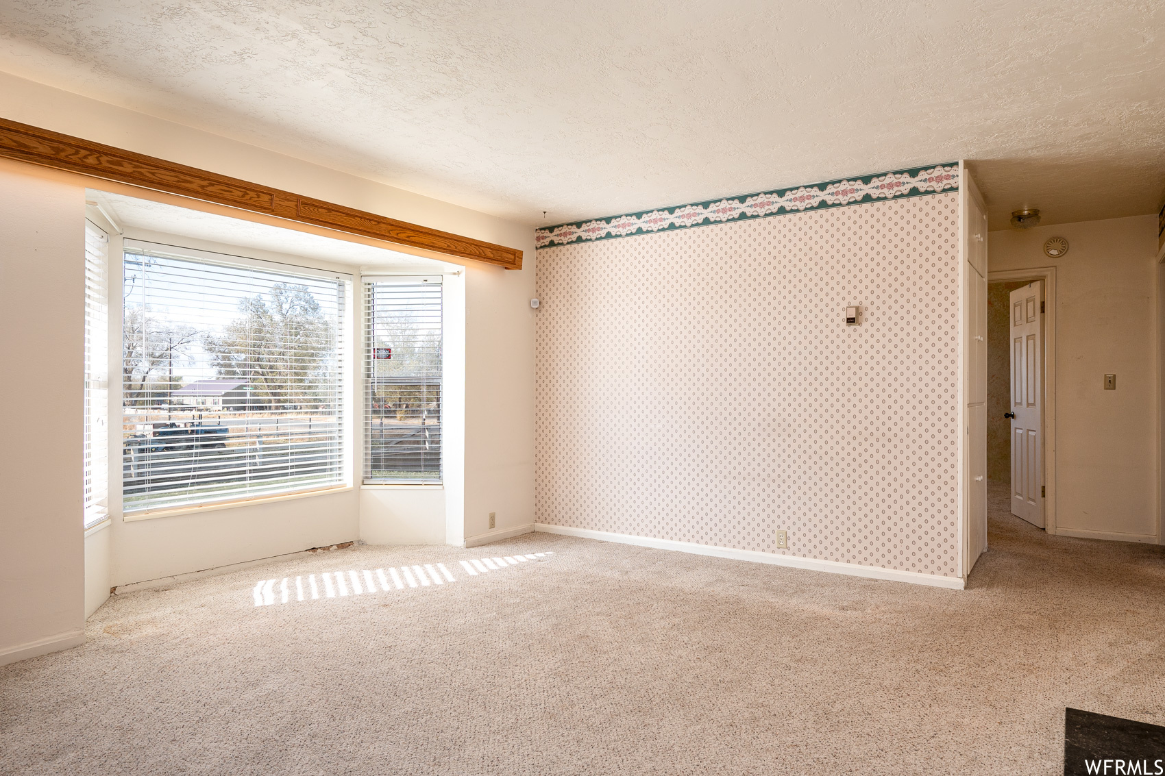 Empty room with light colored carpet and a textured ceiling